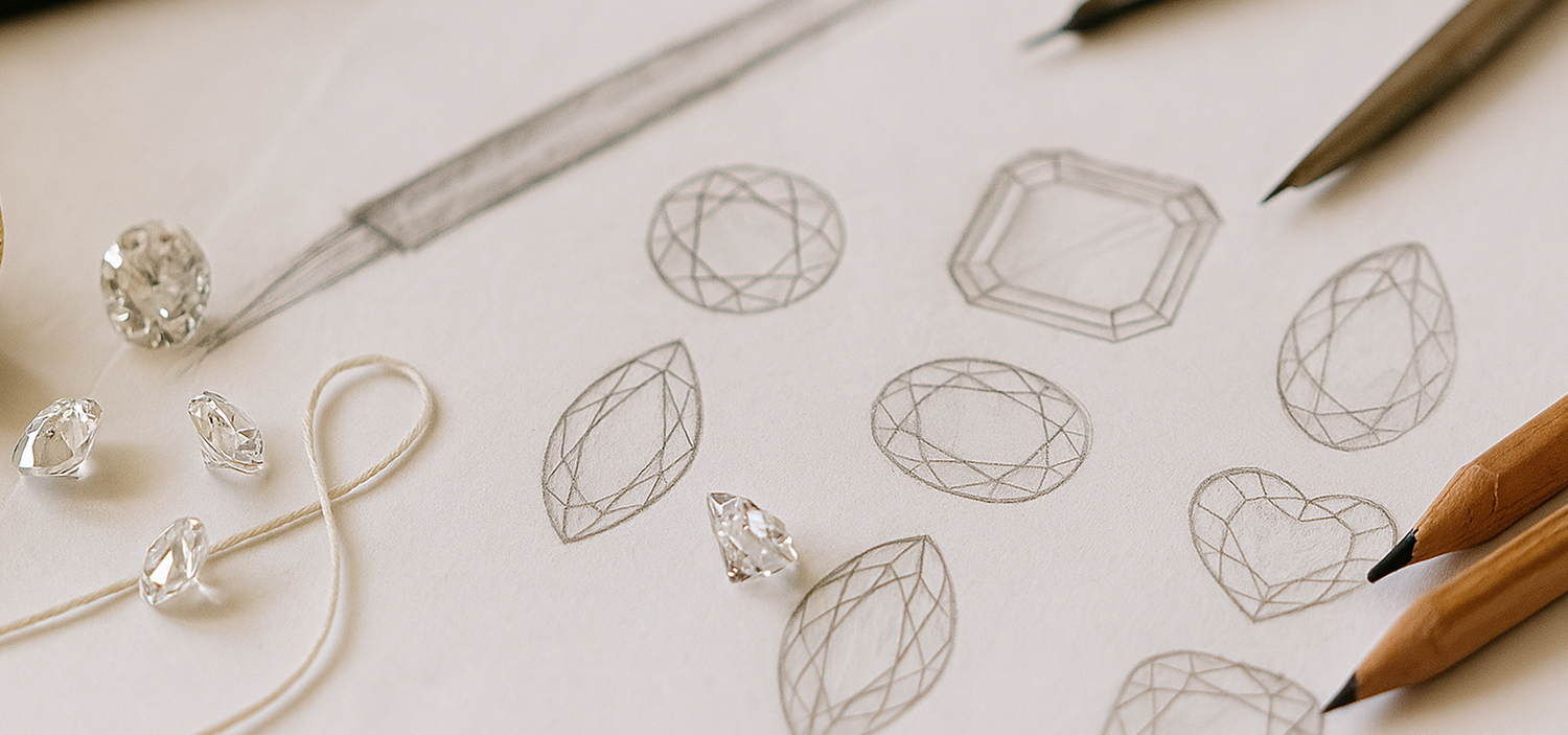 Close-up of a designer's workspace showing jewellery sketches of various diamond cuts, including round, oval, marquise, pear, and heart shapes, alongside several loose lab-grown diamonds and design tools. Emphasizes the custom design process for ethical fine jewellery.
