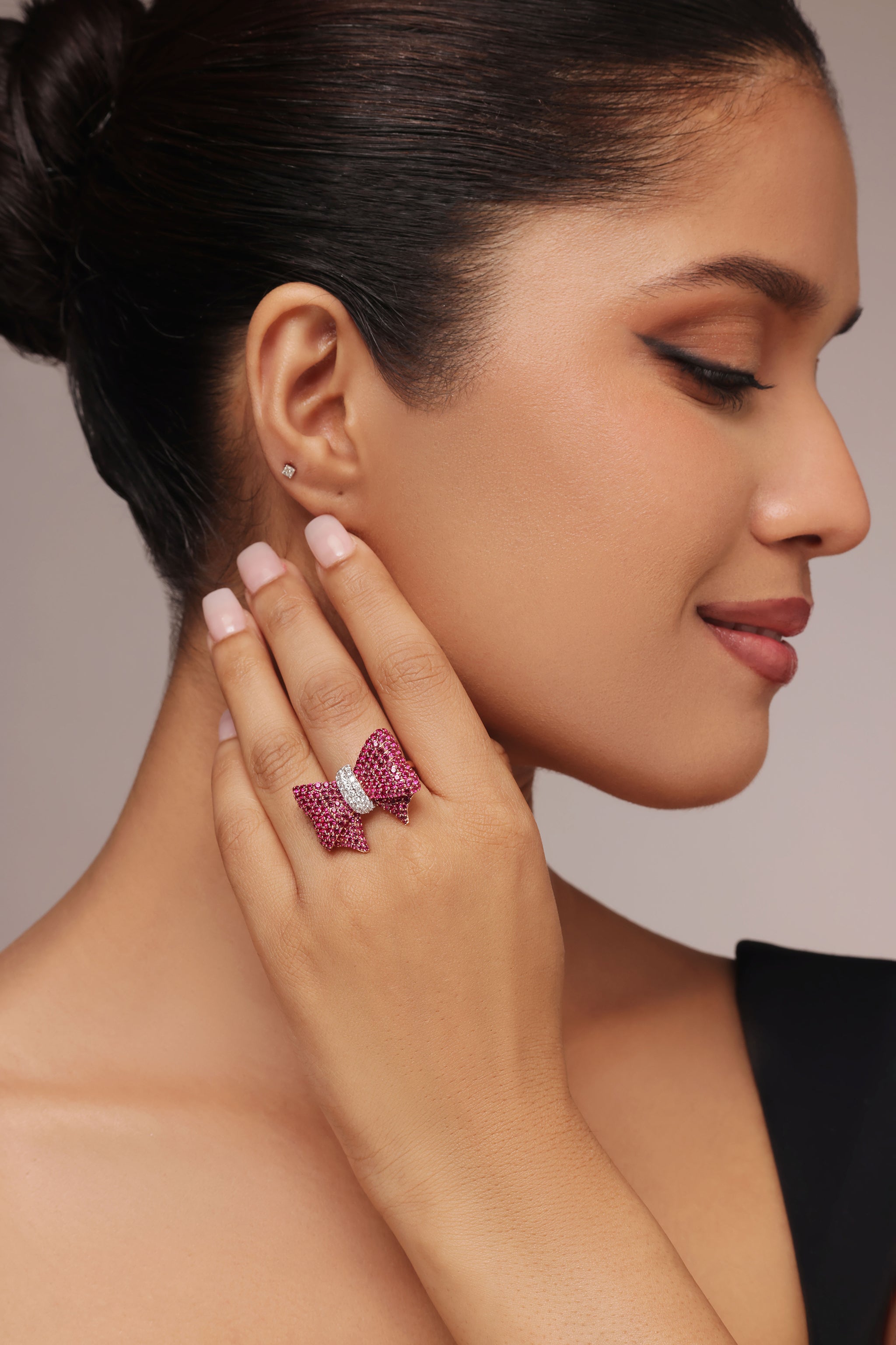 Close-up shot of a hand modeling a playful female ring with a bow design. The ring features rubies on the sides and a center knot area pavé-set with round diamonds in center, all featuring lab grown diamond in it.
