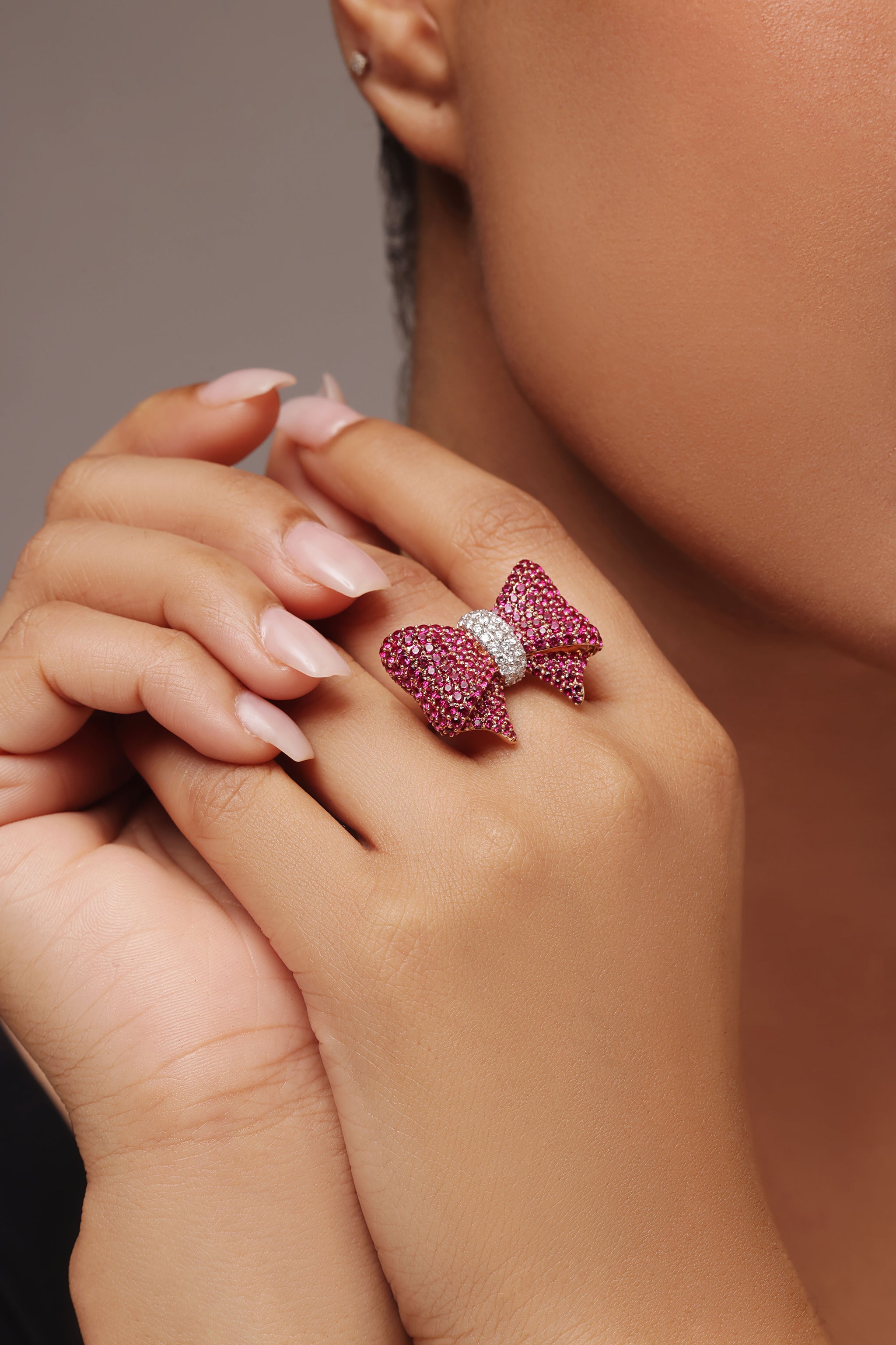 Close-up shot of a hand modeling a playful female ring with a bow design. The ring features rubies on the sides and a center knot area pavé-set with round diamonds in center, all featuring lab grown diamond in it.