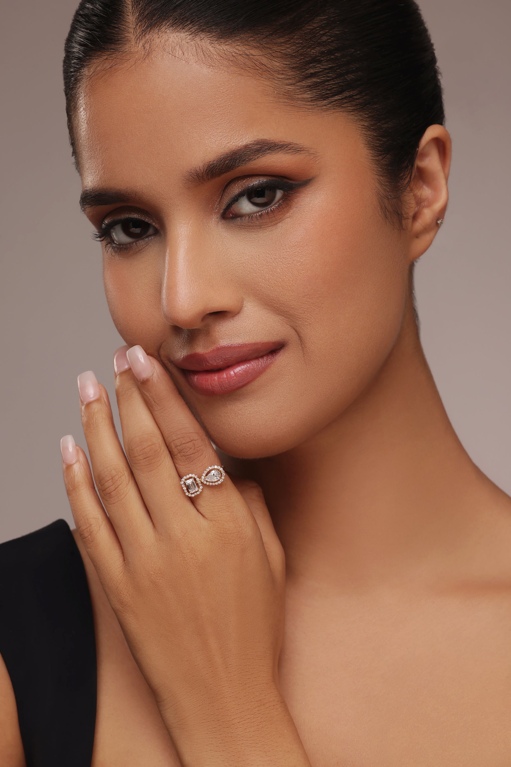 Close-up shot of a hand modeling a toi et moi ring with lab grown diamond in it, featuring a pear-shaped diamond and an emerald-cut diamond, each surrounded by a round halo.