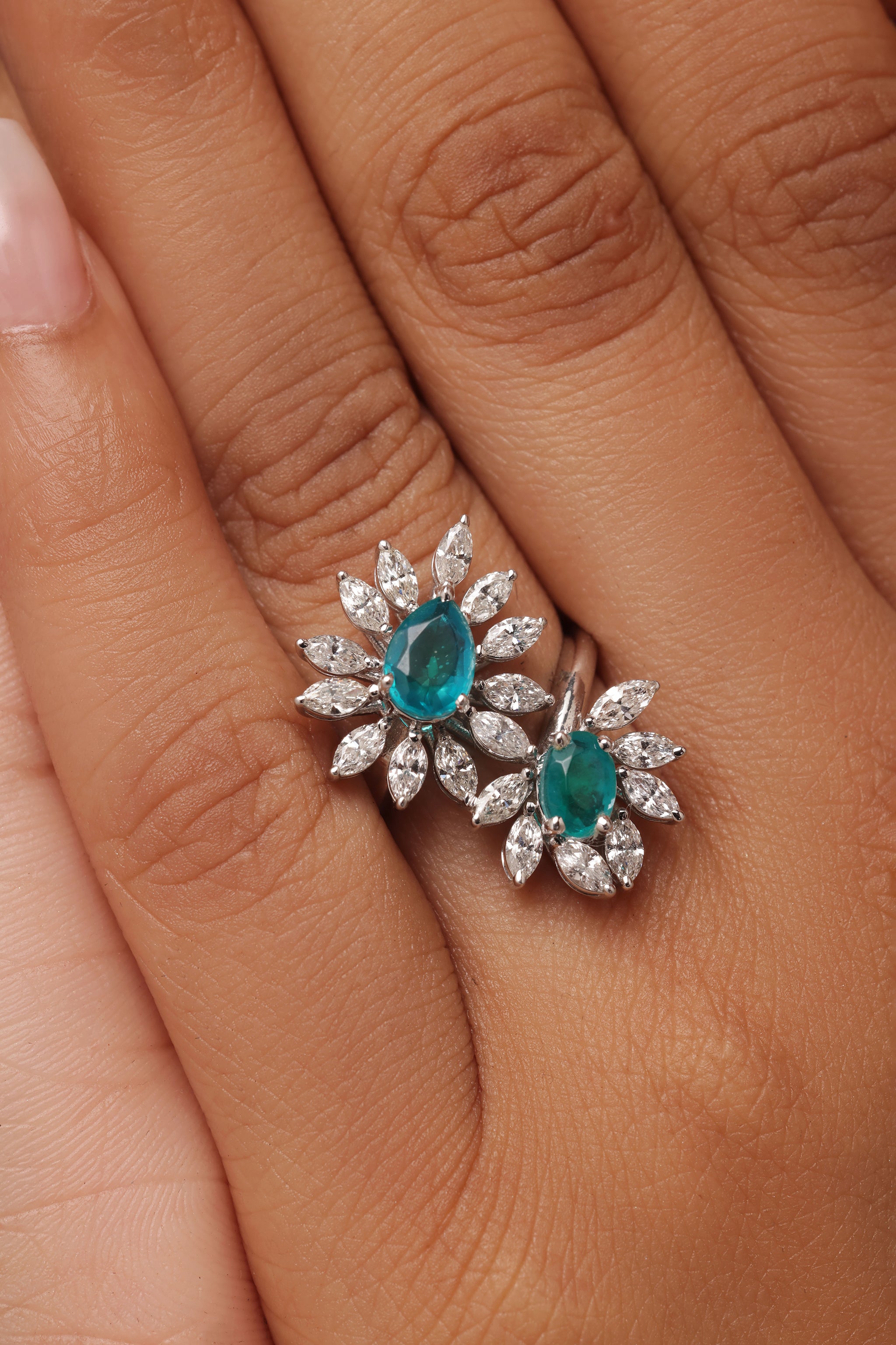 Close-up shot of a hand modeling a bold female ring with lab grown diamond in it. The design features two clusters, each centered with a green stone (oval-shaped), surrounded by a dazzling array of pear and marquise diamonds.