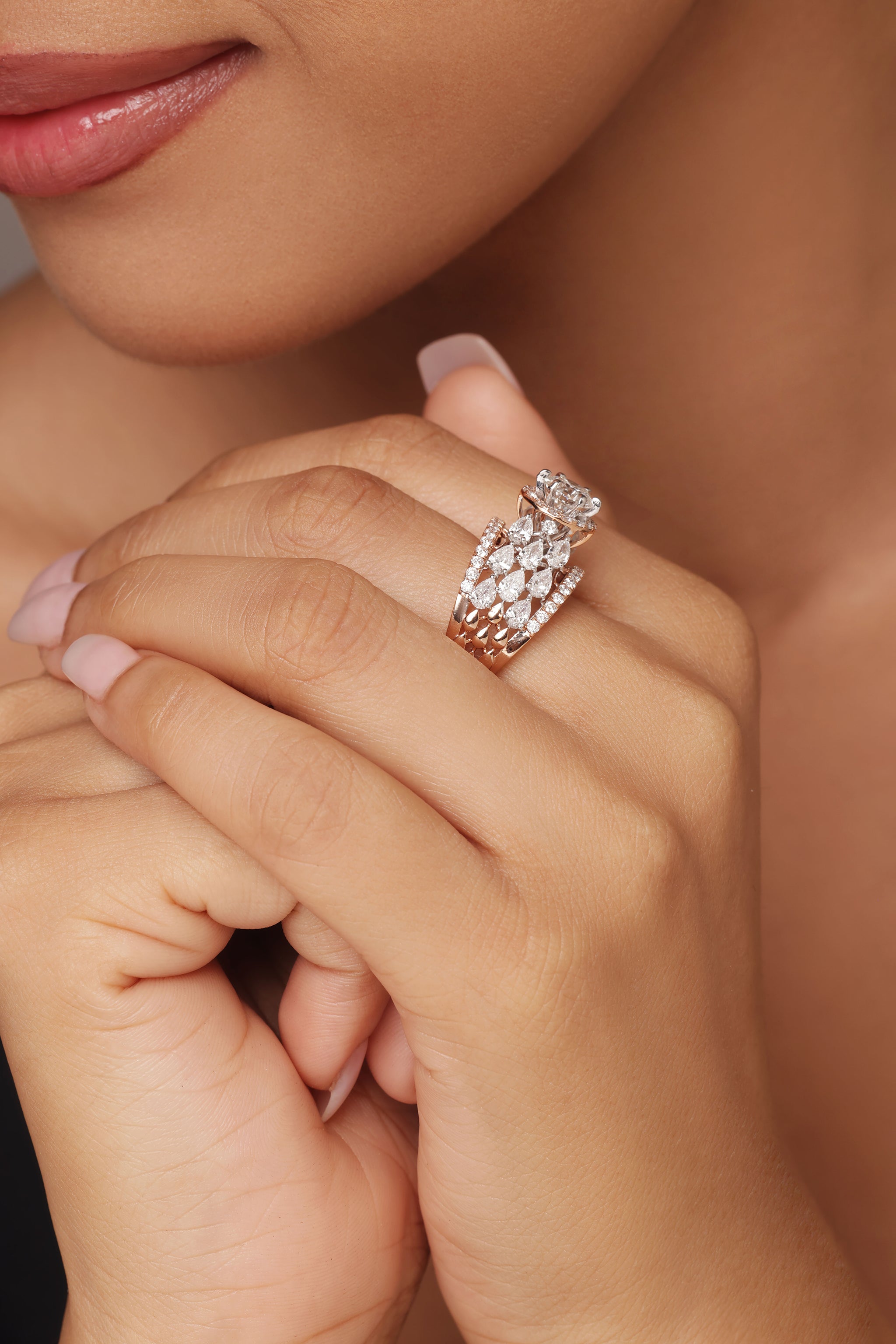Close-up shot of a hand modeling a luxurious ring with lab grown diamond in it. The design features a cluster that gives the effect of a round diamond with halo, and is surrounded by smaller, dazzling clusters that act as pear accents, all set on a rose gold pavé band.