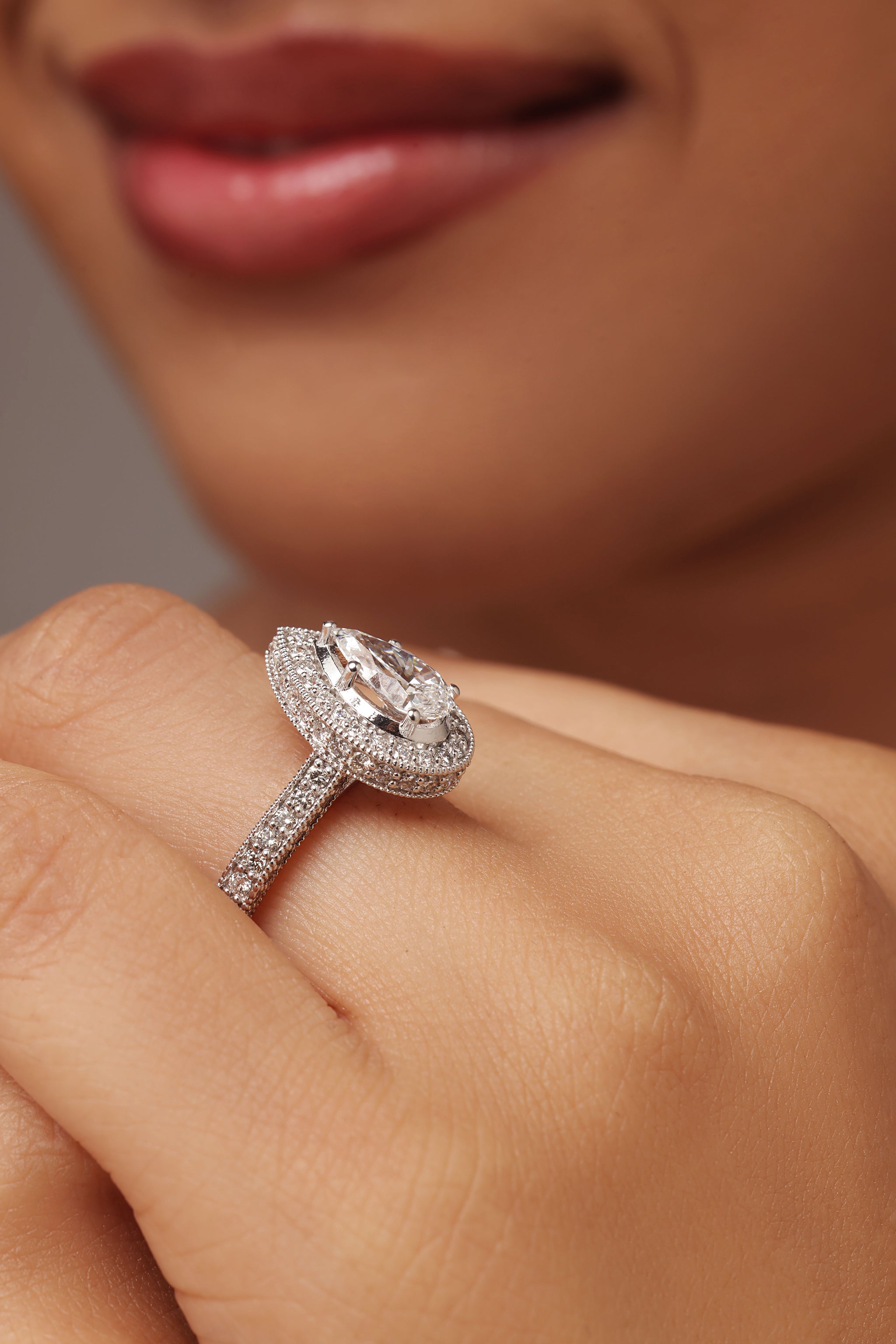 Close-up shot of a hand modeling an engagement-style ring with a pear diamond center stone, surrounded by a halo and set on a round diamond pave band, featuring lab grown diamond in it.