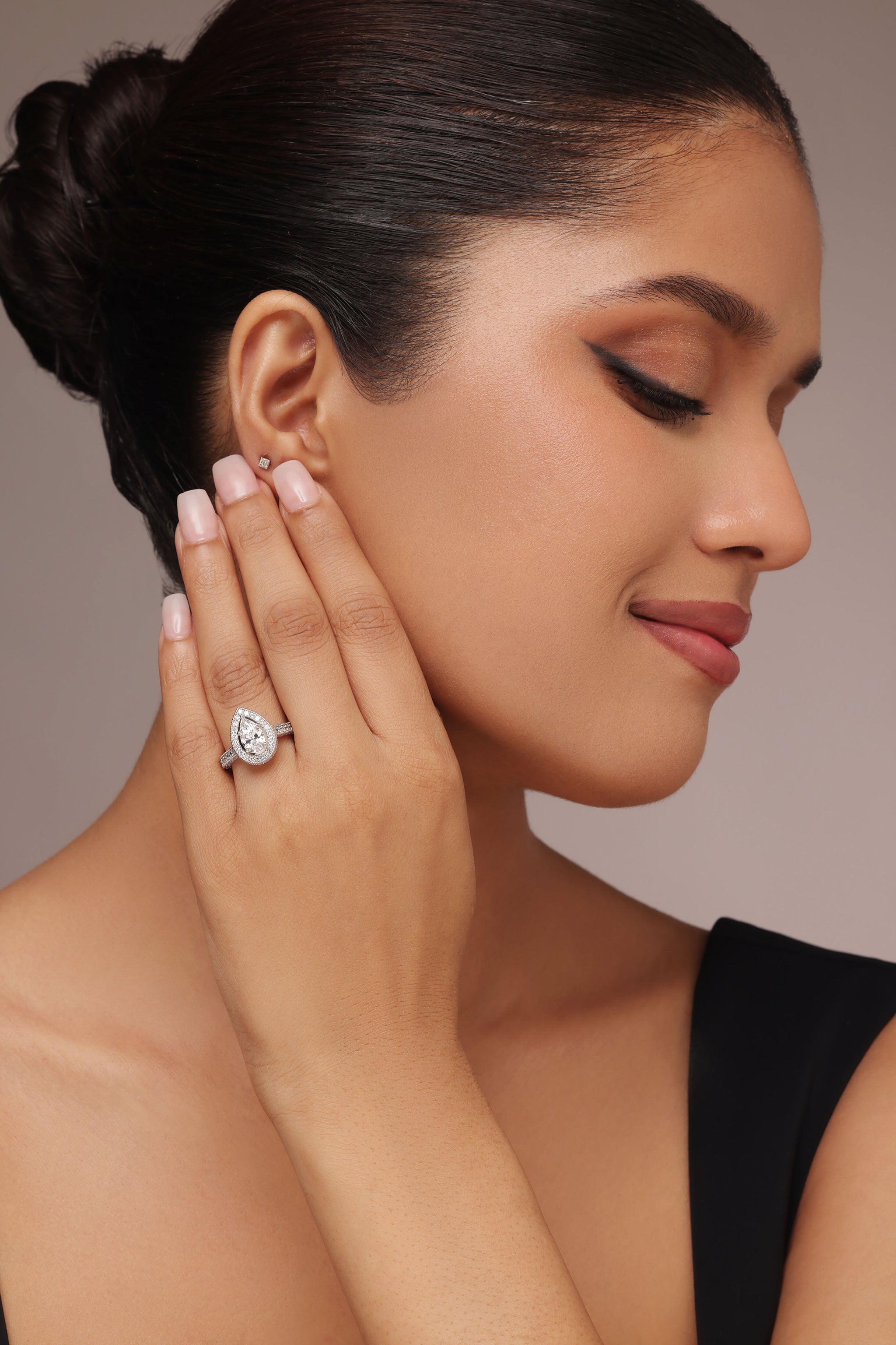 Close-up shot of a hand modeling an engagement-style ring with a pear diamond center stone, surrounded by a halo and set on a round diamond pave band, featuring lab grown diamond in it.