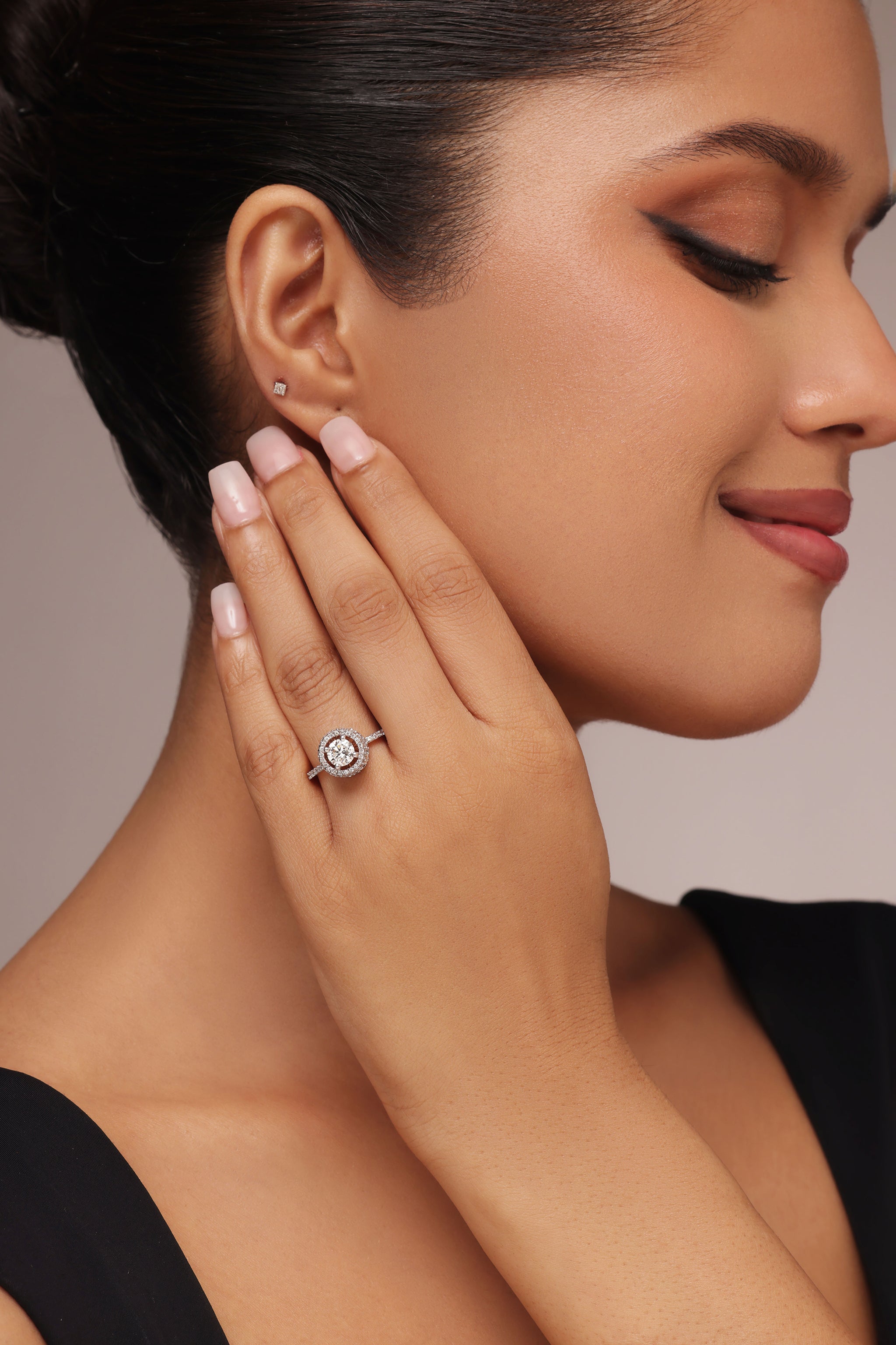 Close-up shot of a hand modeling a large female ring with a round solitaire center stone and lab grown diamond in it. The design features a double halo with multiple marquise-shaped stones around the sides, set on a pavé band.