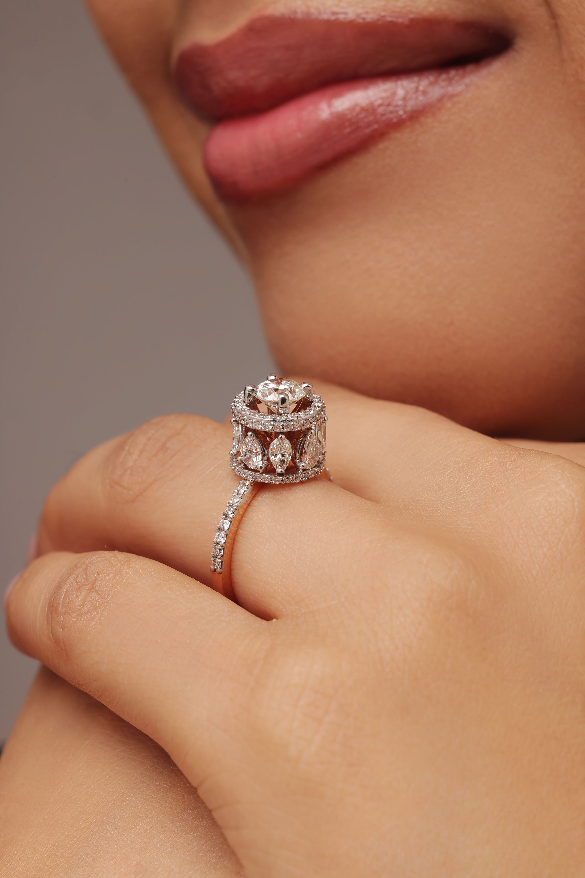 Close-up shot of a hand modeling a large female ring with a round solitaire center stone and lab grown diamond in it. The design features a double halo with multiple marquise-shaped stones around the sides, set on a pavé band.