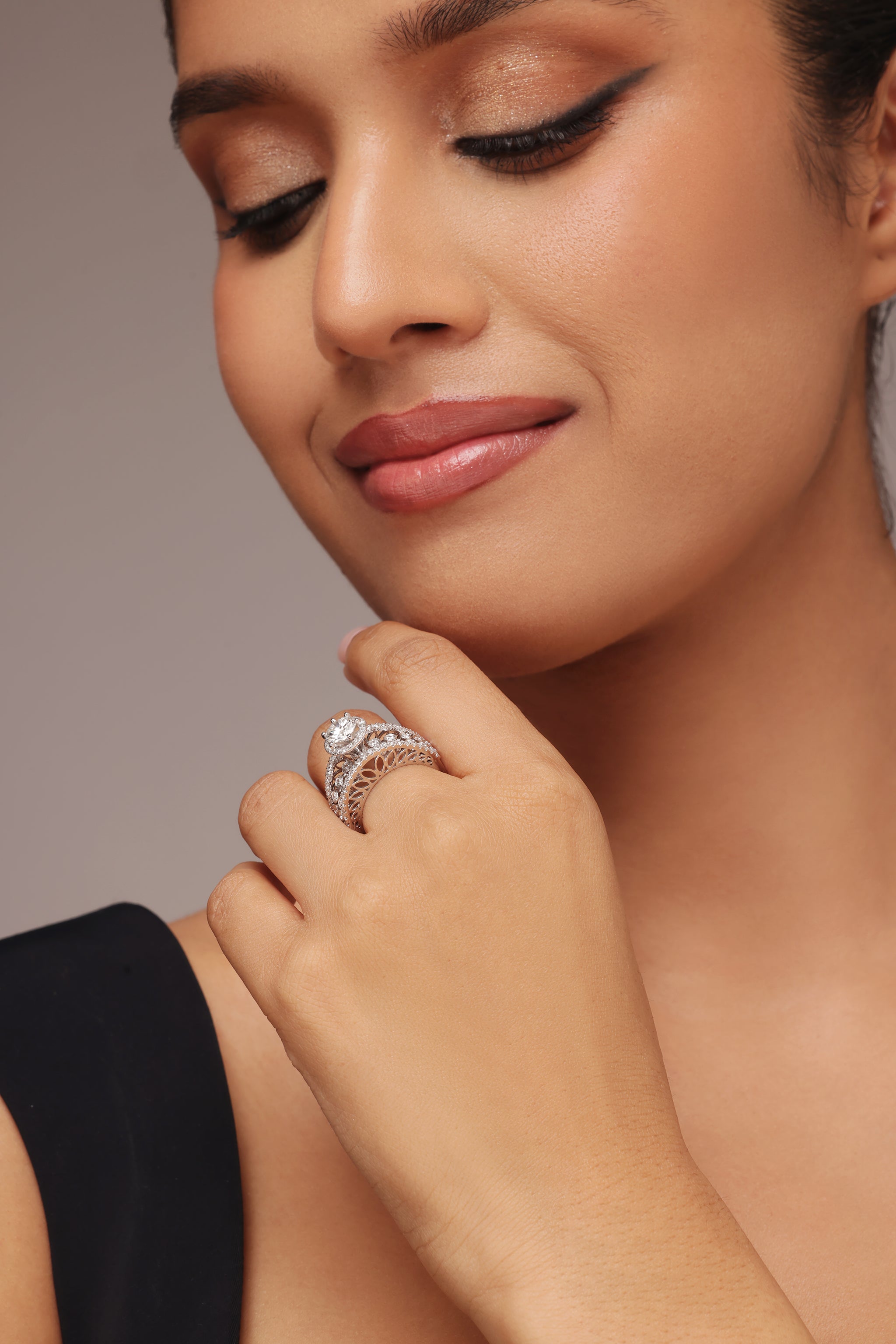 Close-up shot of a hand modeling an elaborate wide ring with round diamond all the way and lab grown diamond in it. The ring features a round diamond center stone with a halo, set next to an ornate band made of decorative diamond clusters and lattice work.