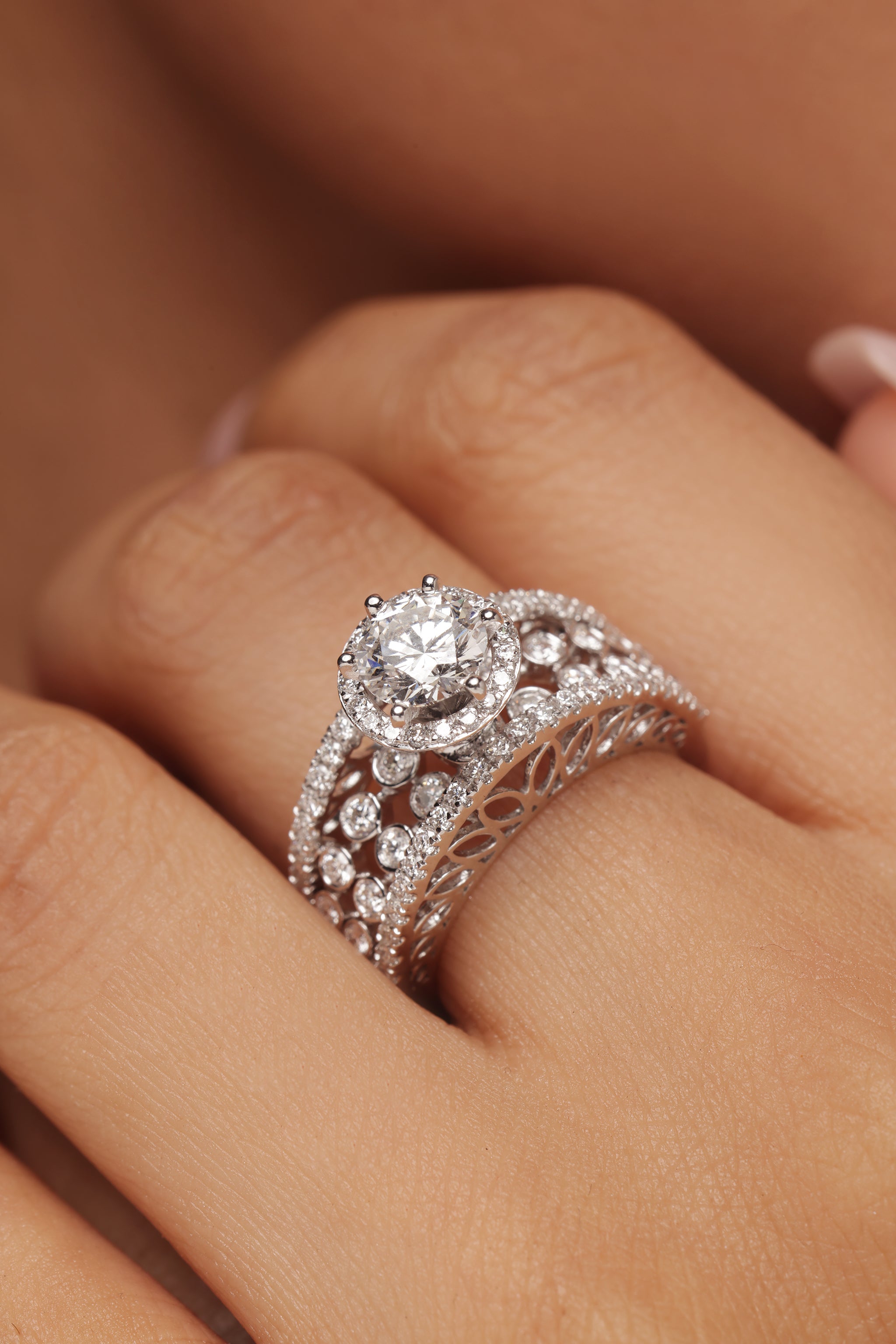 Close-up shot of a hand modeling an elaborate wide ring with round diamond all the way and lab grown diamond in it. The ring features a round diamond center stone with a halo, set next to an ornate band made of decorative diamond clusters and lattice work.