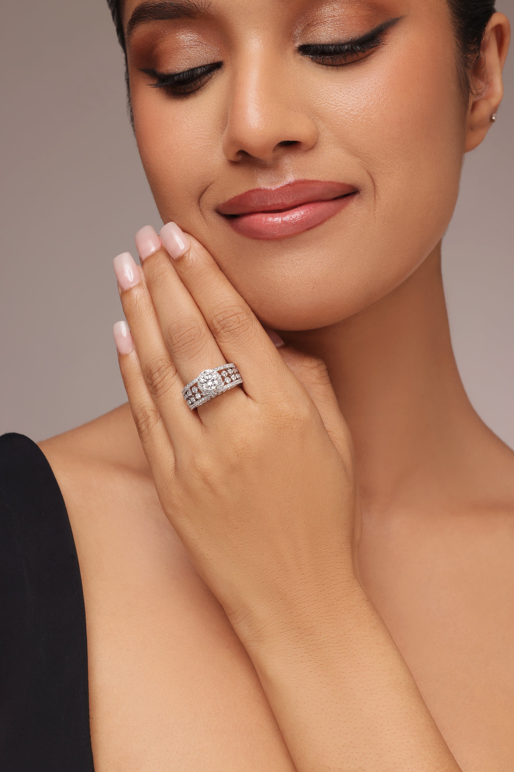 Close-up shot of a hand modeling an elaborate wide ring with round diamond all the way and lab grown diamond in it. The ring features a round diamond center stone with a halo, set next to an ornate band made of decorative diamond clusters and lattice work.