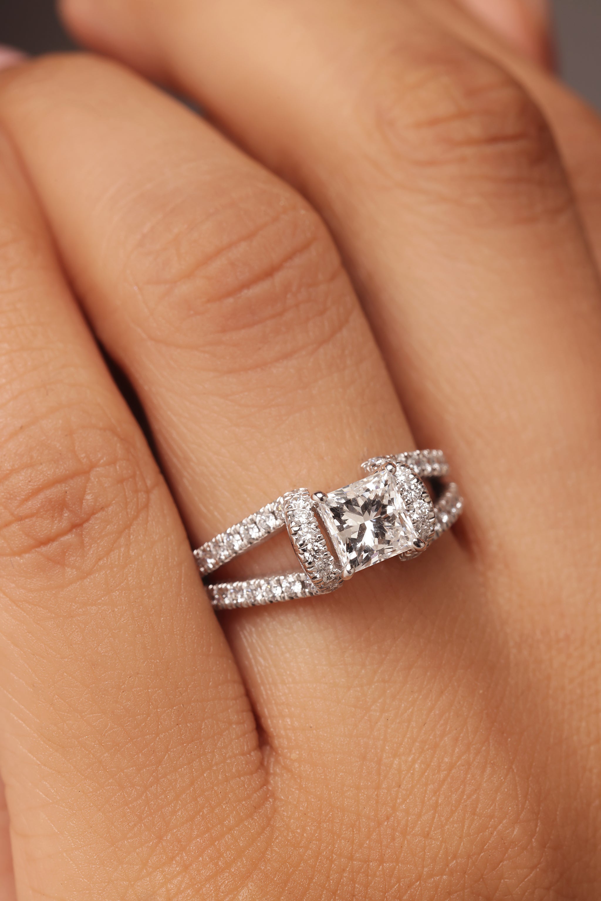 Close-up shot of a hand modeling a ring with a cushion or square-cut center stone and lab grown diamond in it, set in a modern split, pave-set open shank.
