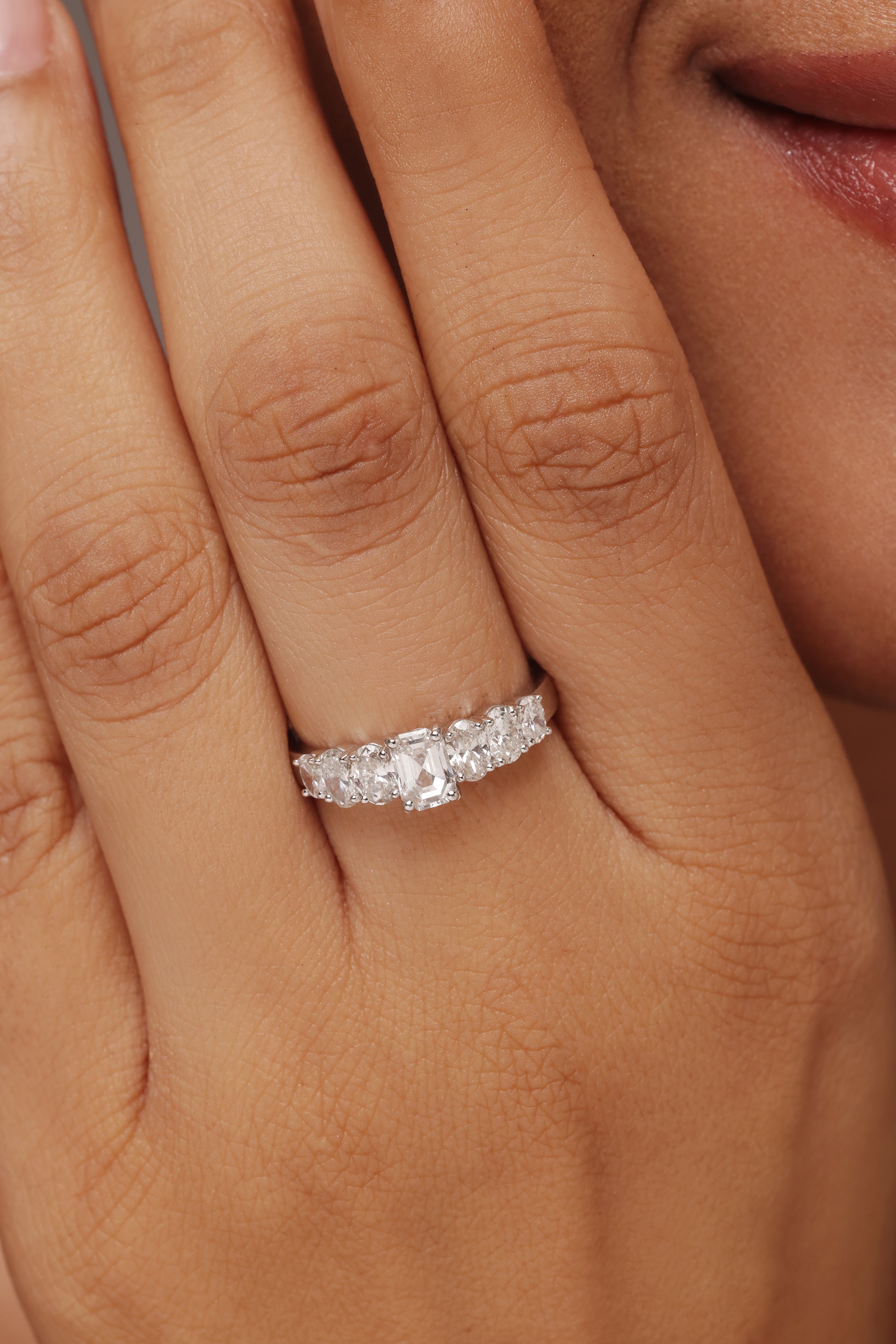 Close-up shot of a hand modeling a sparkling multi-stone band ring with lab grown diamond in it, featuring a large center emerald diamond flanked by smaller oval diamond on either side.