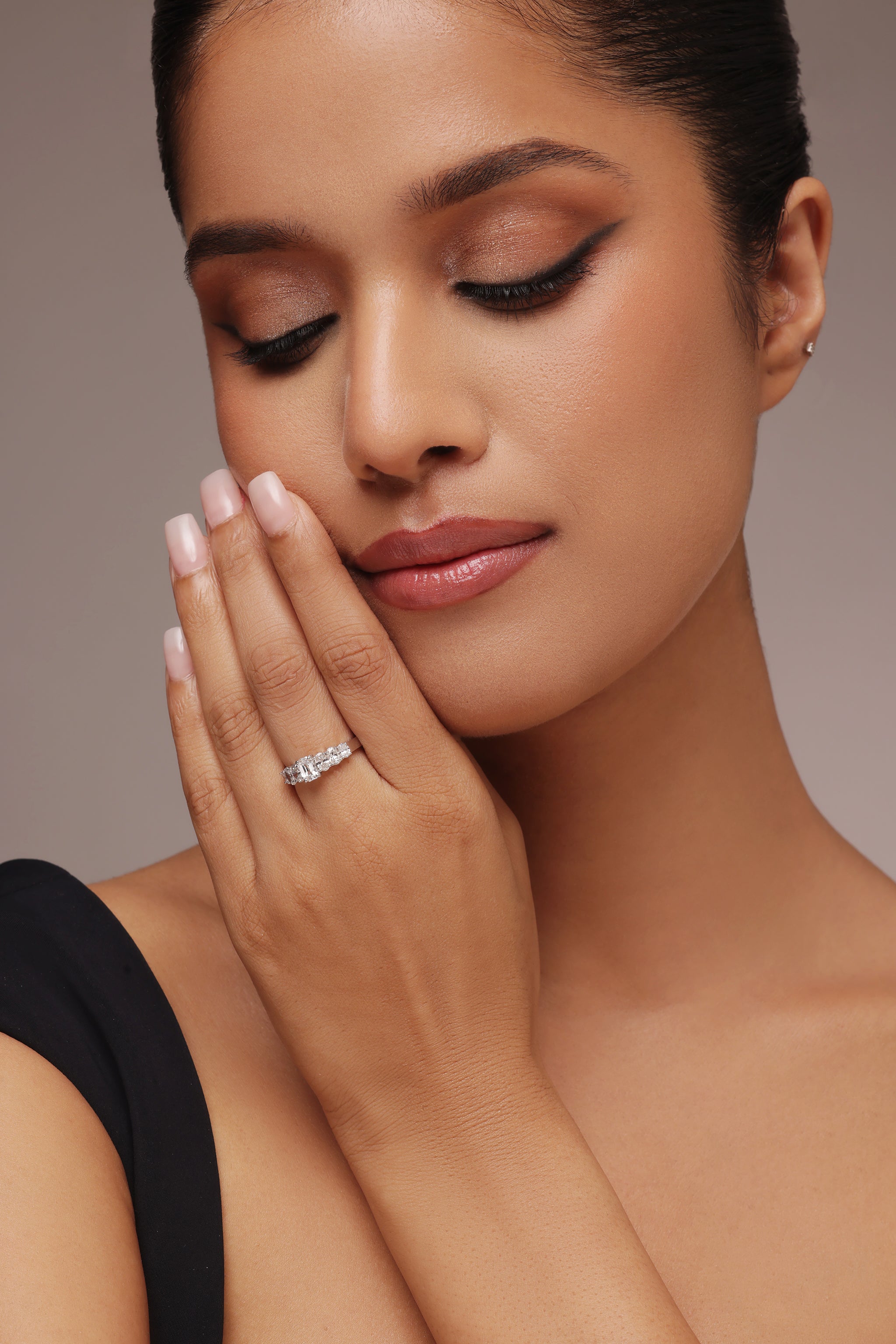 Close-up shot of a hand modeling a sparkling multi-stone band ring with lab grown diamond in it, featuring a large center stone flanked by smaller clear stones on either side.
