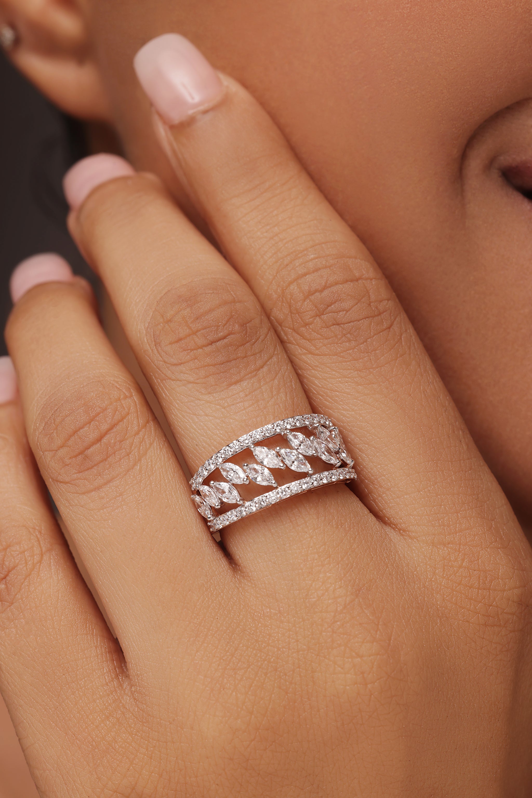Close-up shot of a hand modeling a wide female ring with lab grown diamond in it, featuring a layered design of pavé-set round diamond borders and a central row of marquise diamonds.
