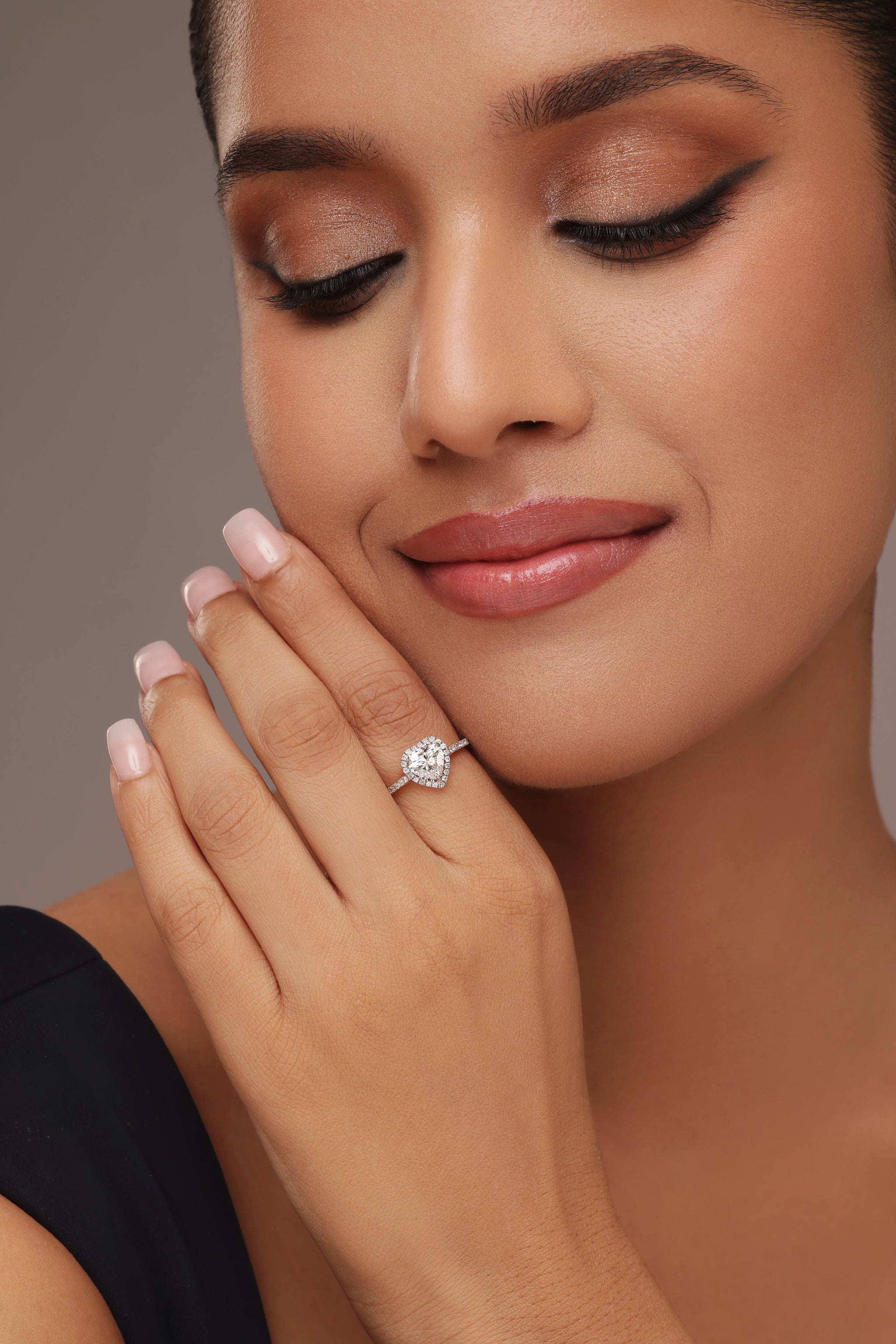 Close-up shot of a hand modeling a ring with a heart-shaped lab grown diamond in it center stone, surrounded by a round halo and set on a round pave band.
