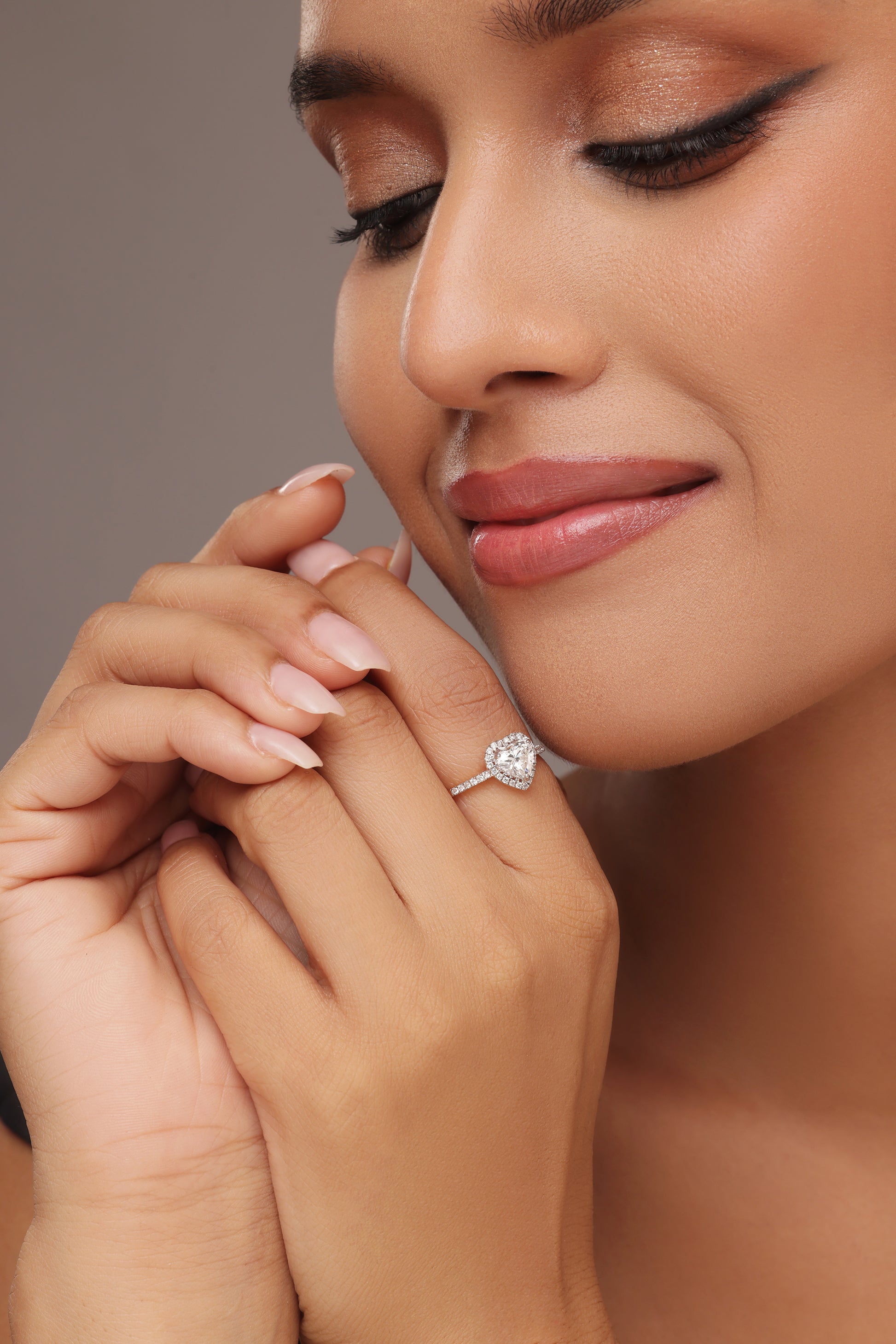 Close-up shot of a hand modeling a ring with a heart-shaped lab grown diamond in it center stone, surrounded by a round halo and set on a round pave band.