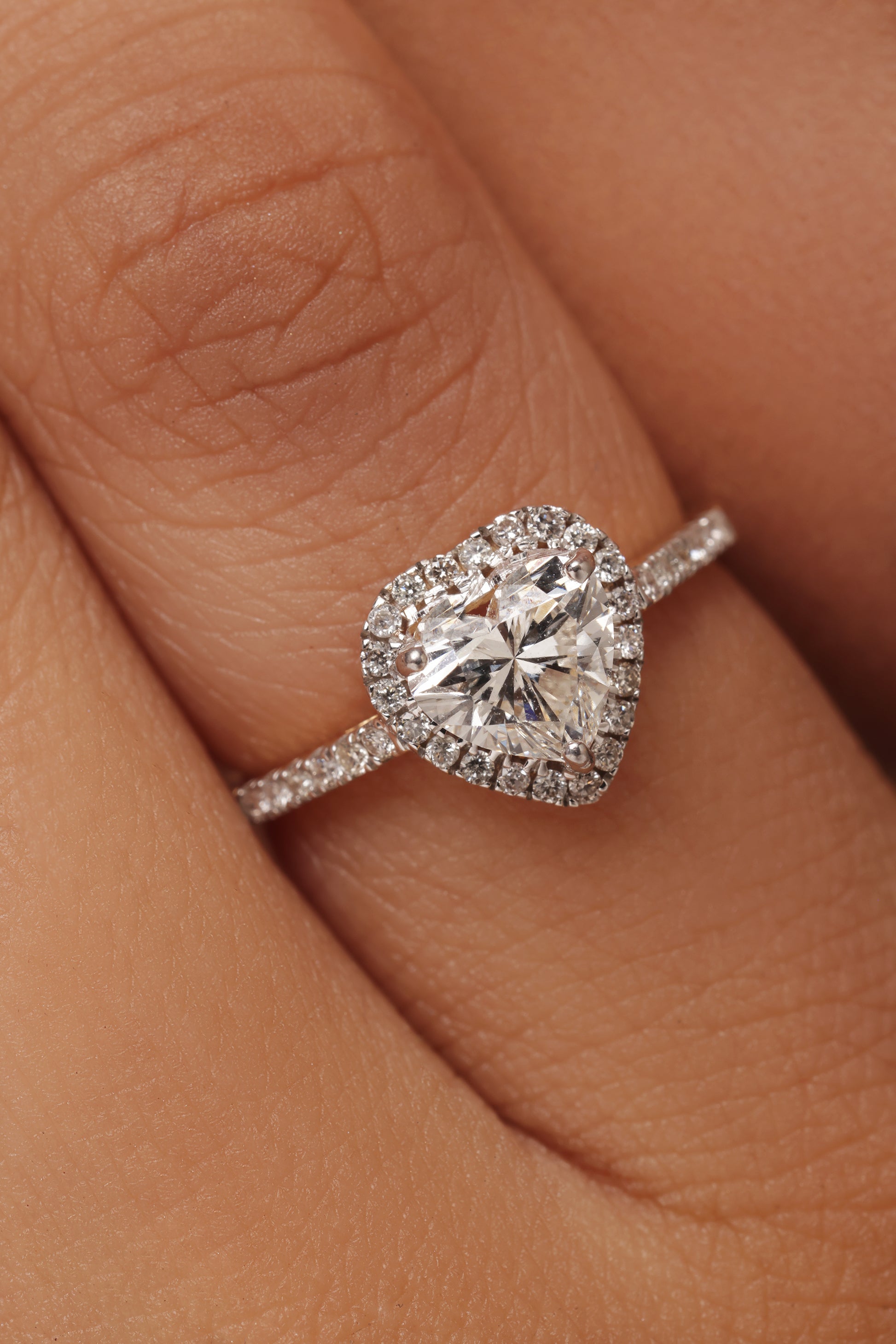Close-up shot of a hand modeling a ring with a heart-shaped lab grown diamond in it center stone, surrounded by a round halo and set on a round pave band.