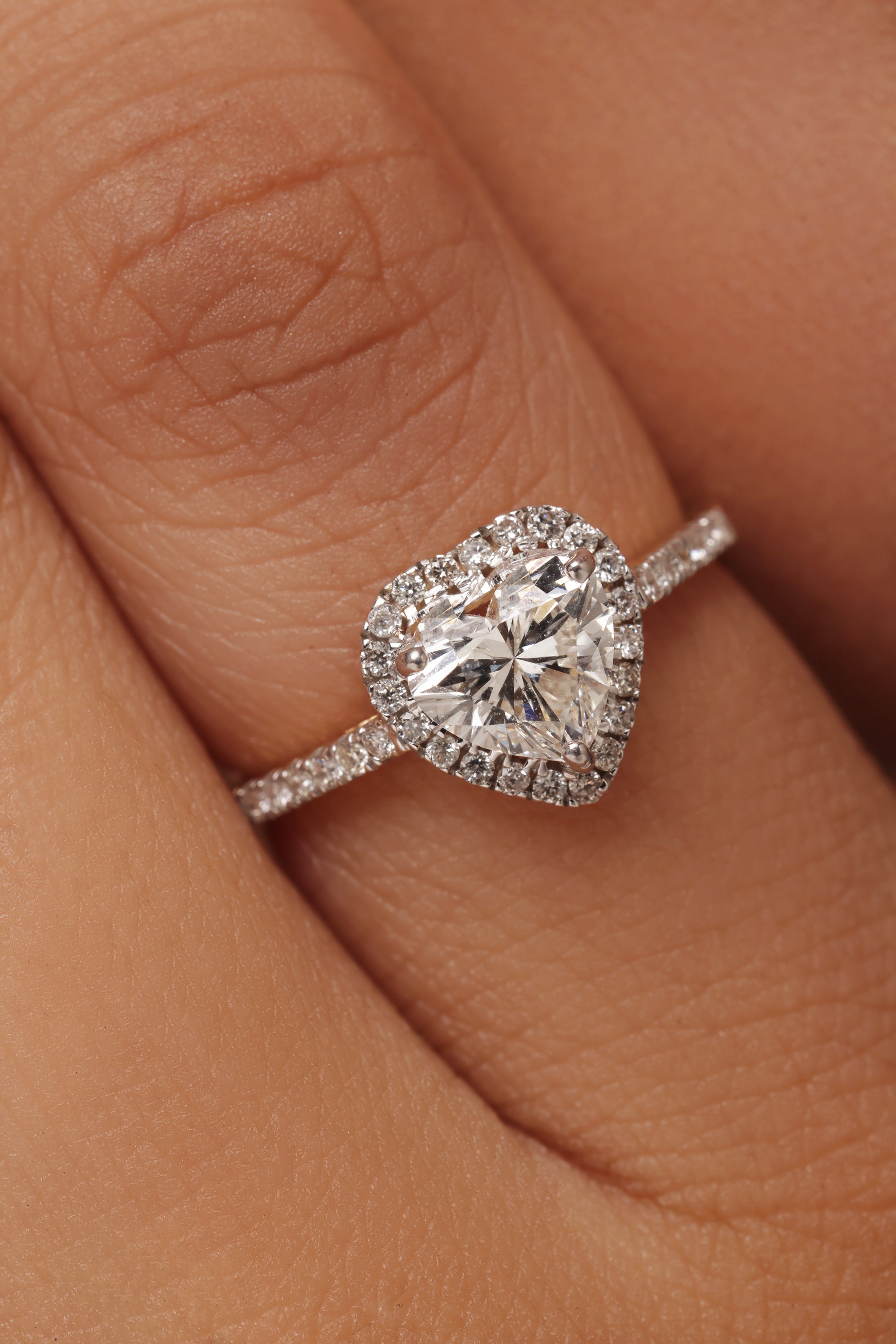 Close-up shot of a hand modeling a ring with a heart-shaped lab grown diamond in it center stone, surrounded by a round halo and set on a round pave band.