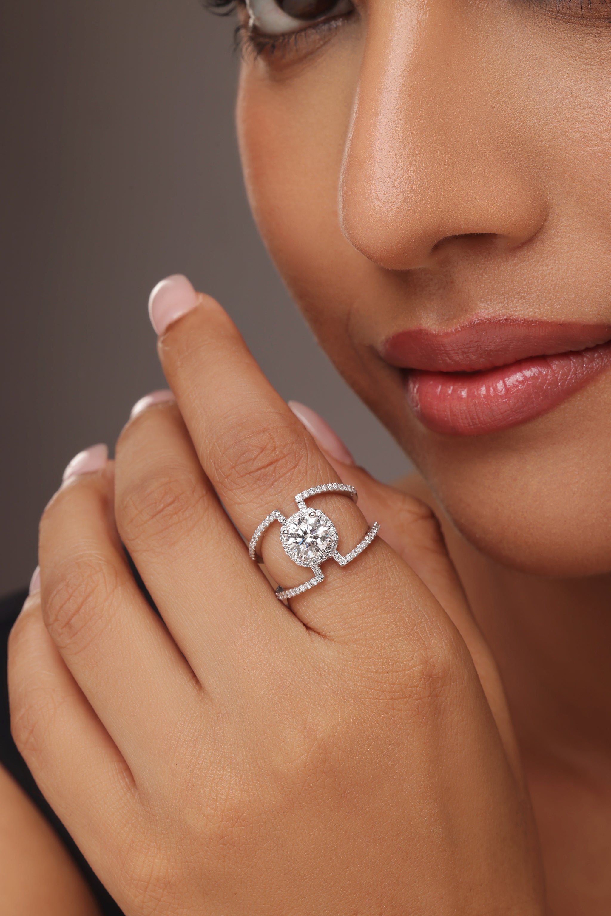 Close-up shot of a hand modeling a unique ring with a round diamond center stone and lab grown diamond in it, set in a modern open shank setting with split, pave-set bands.