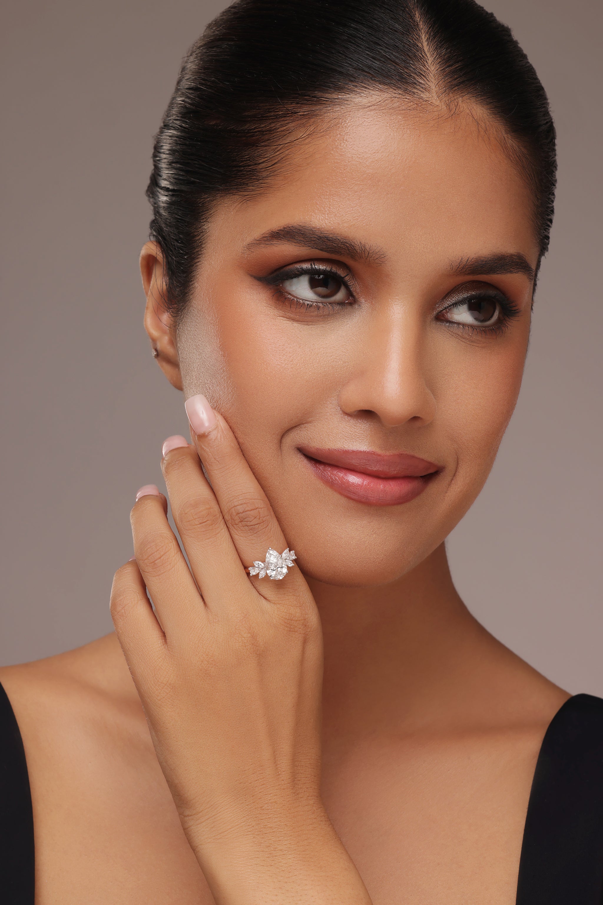 Close-up shot of a hand modeling an elegant ring with lab grown diamond in it, showcasing a large pear-shaped center diamond flanked by smaller marquise-cut diamond or leaf-shaped accent diamonds.
