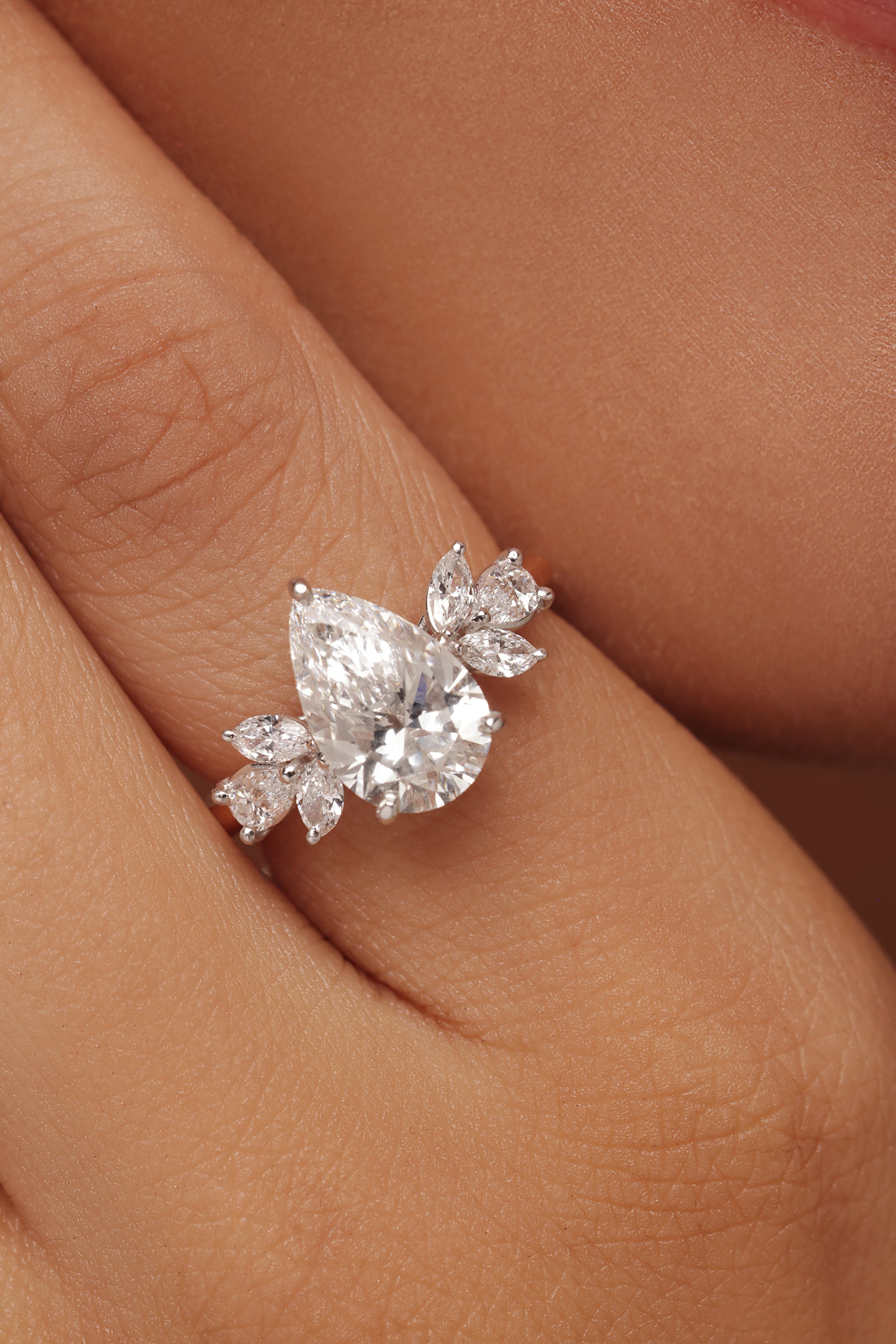 Close-up shot of a hand modeling an elegant ring with lab grown diamond in it, showcasing a large pear-shaped center diamond flanked by smaller marquise-cut diamond or leaf-shaped accent diamonds.