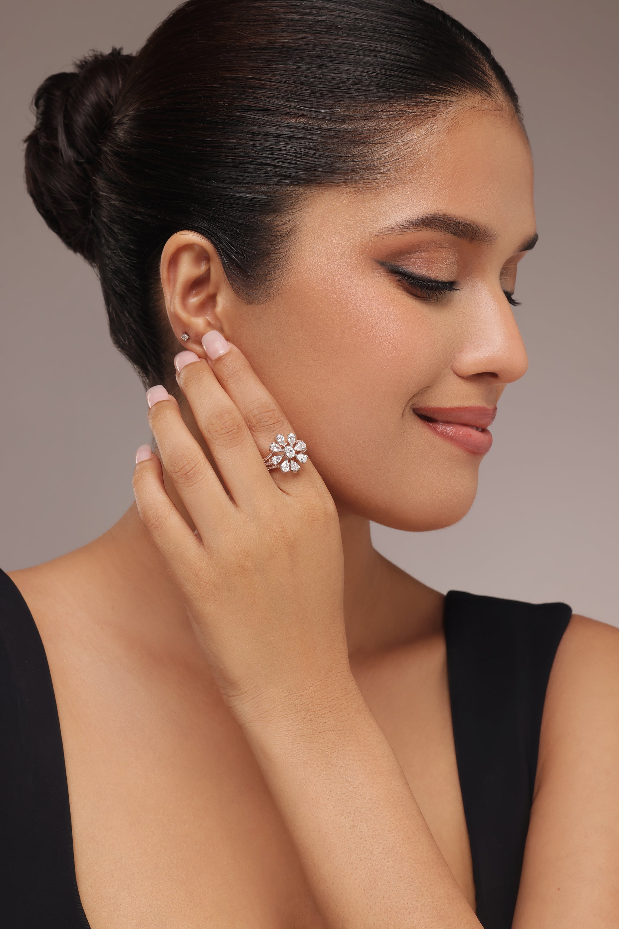 Close-up shot of a hand modeling a ring with lab grown diamond in it, featuring a large flower shape created by surrounding an oval center stone with multiple pear diamond petals, all set on a sparkly triple band.