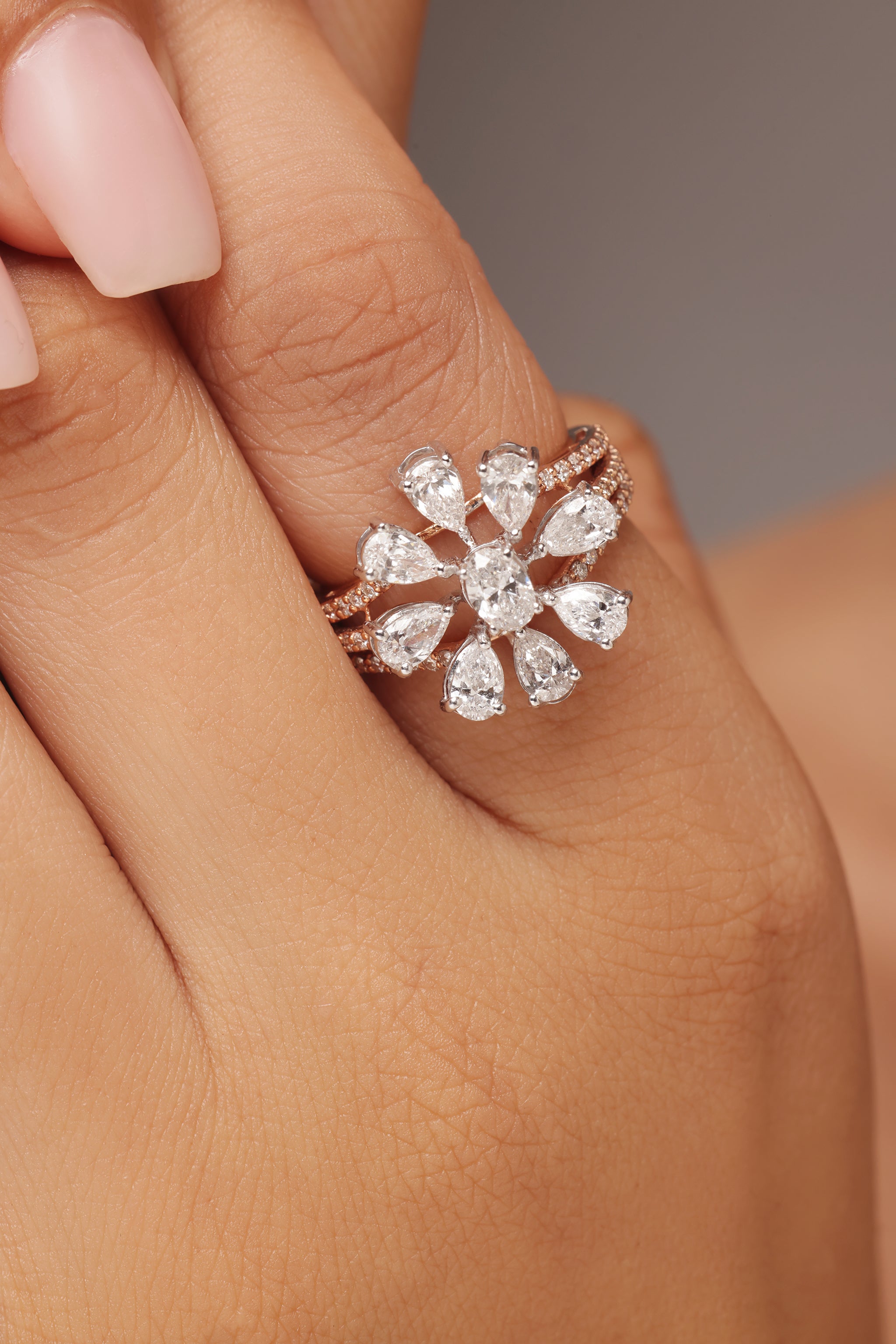 Close-up shot of a hand modeling a ring with lab grown diamond in it, featuring a large flower shape created by surrounding an oval center stone with multiple pear diamond petals, all set on a sparkly triple band.