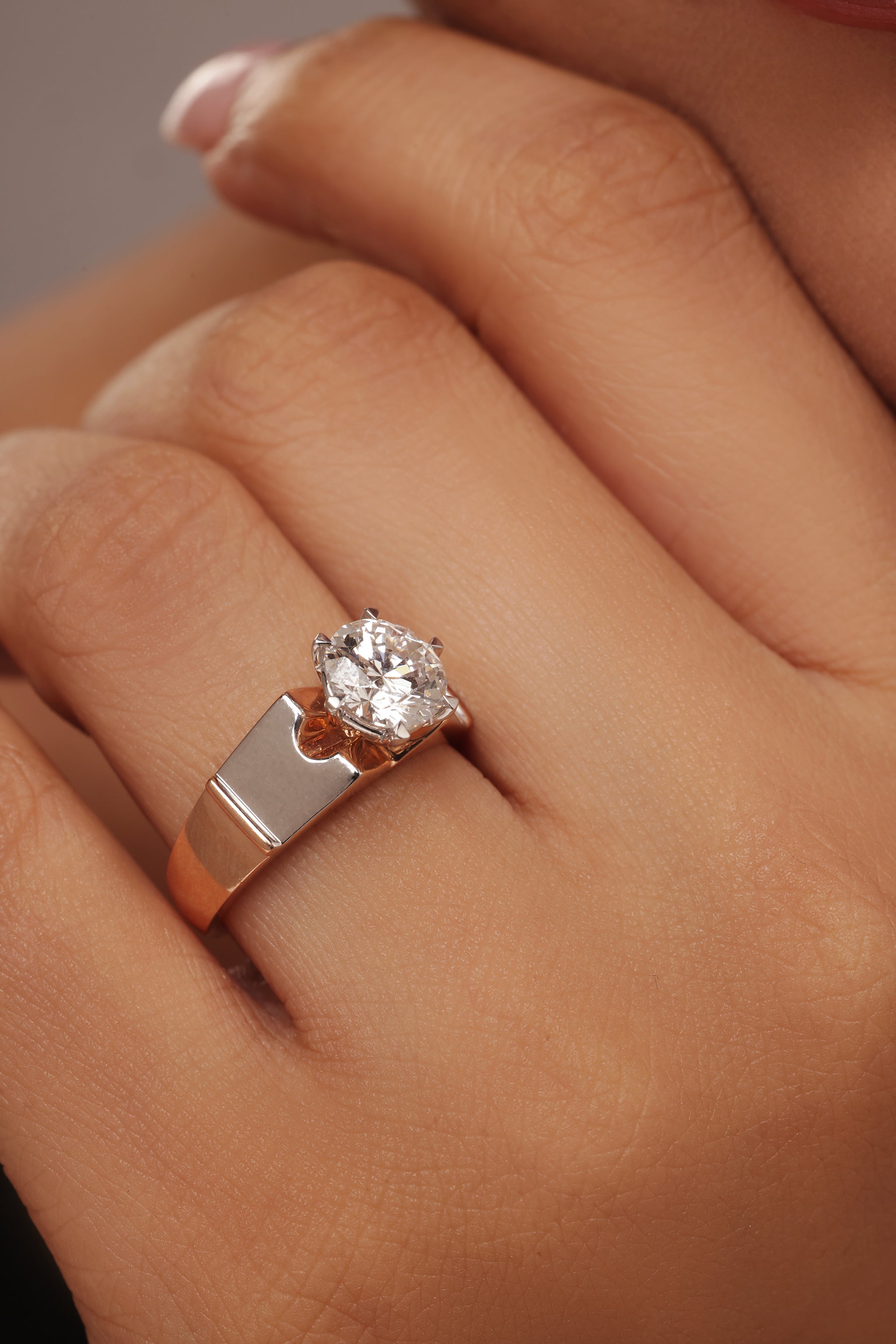 Close-up shot of a hand modeling a female ring with a prominent round lab grown diamond solitaire, set in a modern, wide, two-tone rose gold and silver band.
