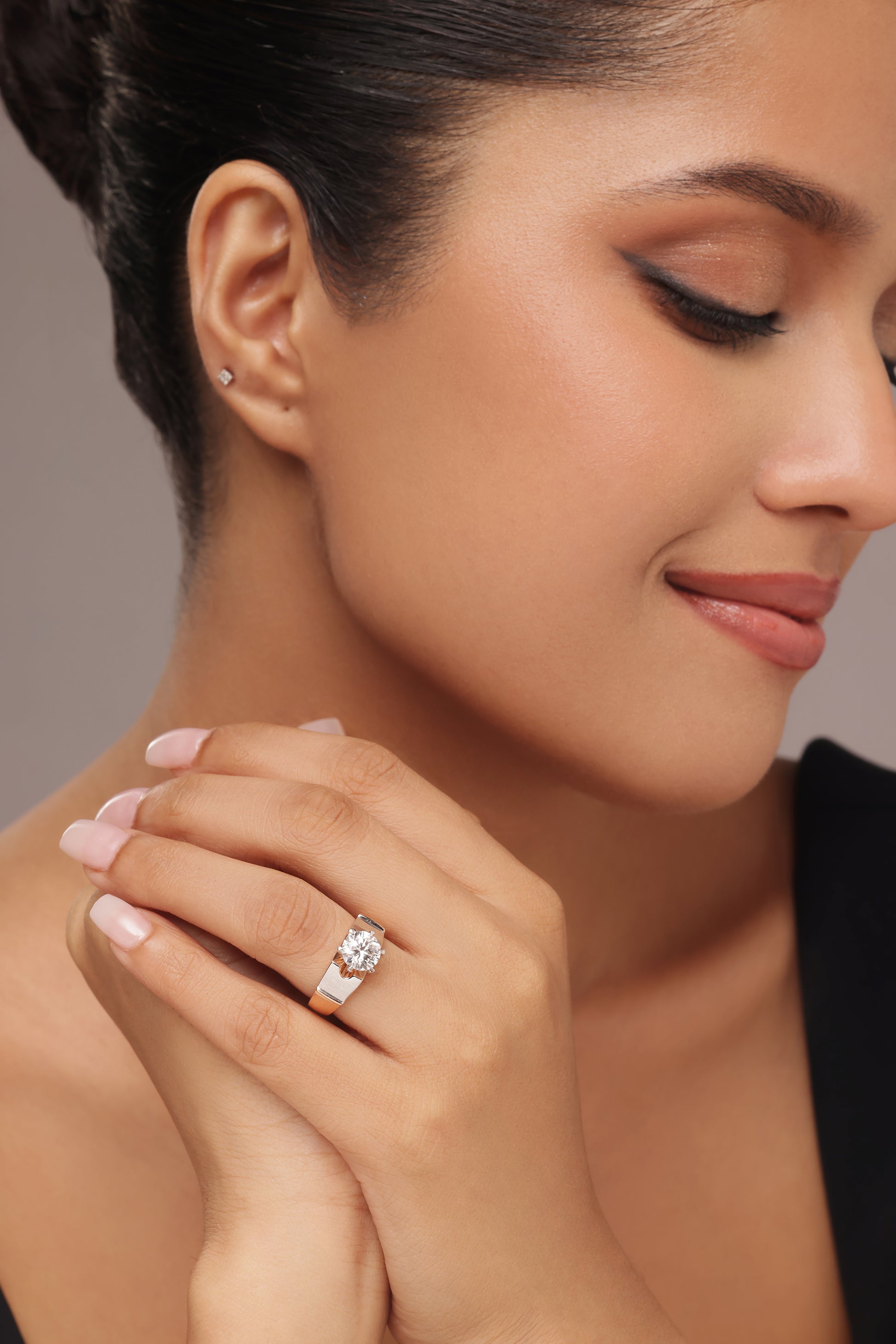 Close-up shot of a hand modeling a female ring with a prominent round lab grown diamond solitaire, set in a modern, wide, two-tone rose gold and silver band.