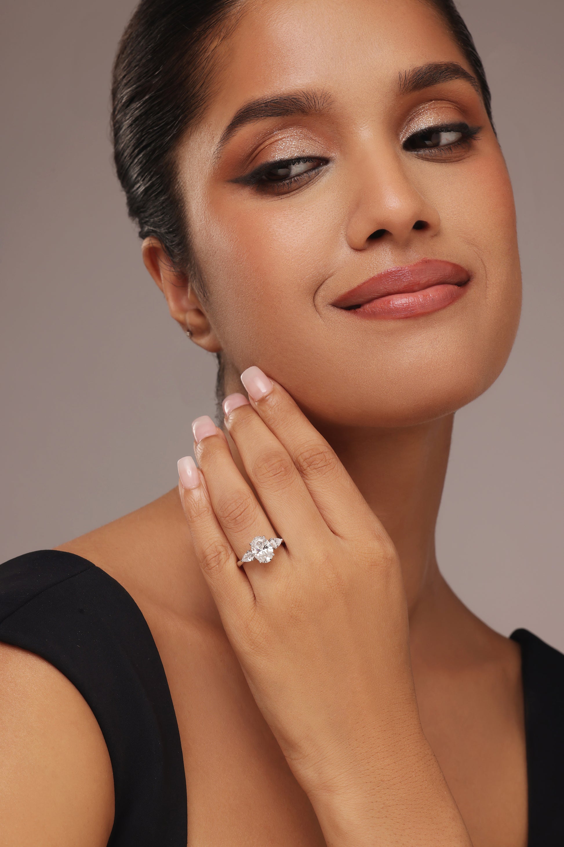 Close-up shot of a hand modeling a female diamond ring with lab grown diamond in it, featuring a prominent oval cut center stone flanked by smaller pear-shaped accent diamonds on a simple band.