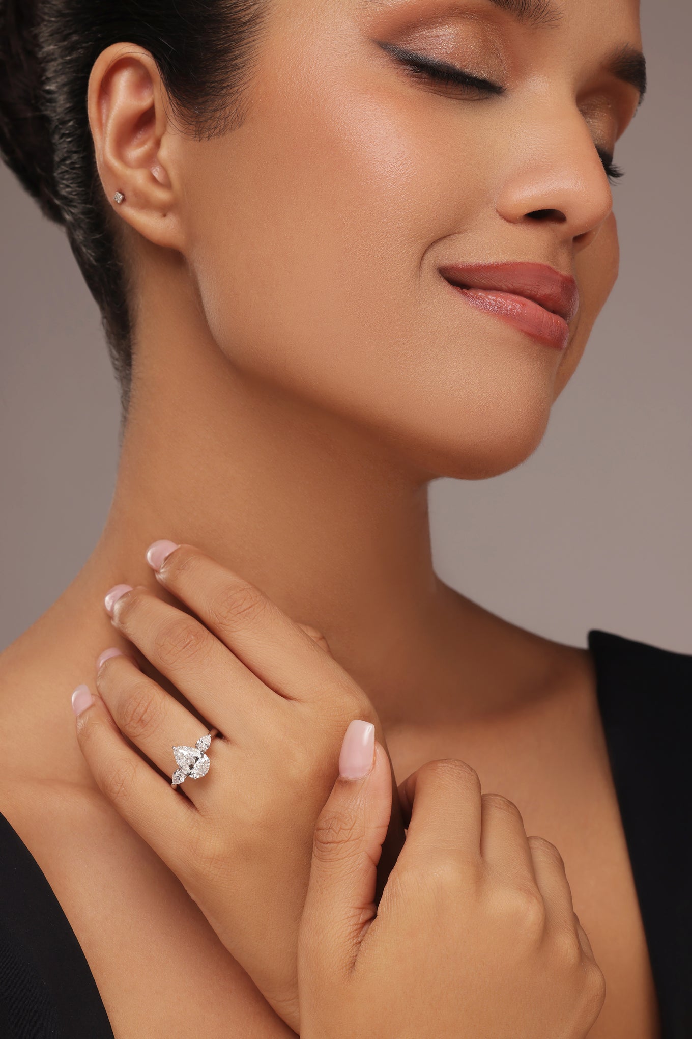 Close-up shot of a hand modeling a female diamond ring with lab grown diamond in it, featuring a prominent pear cut center stone flanked by smaller pear-shaped accent diamonds on a simple band.