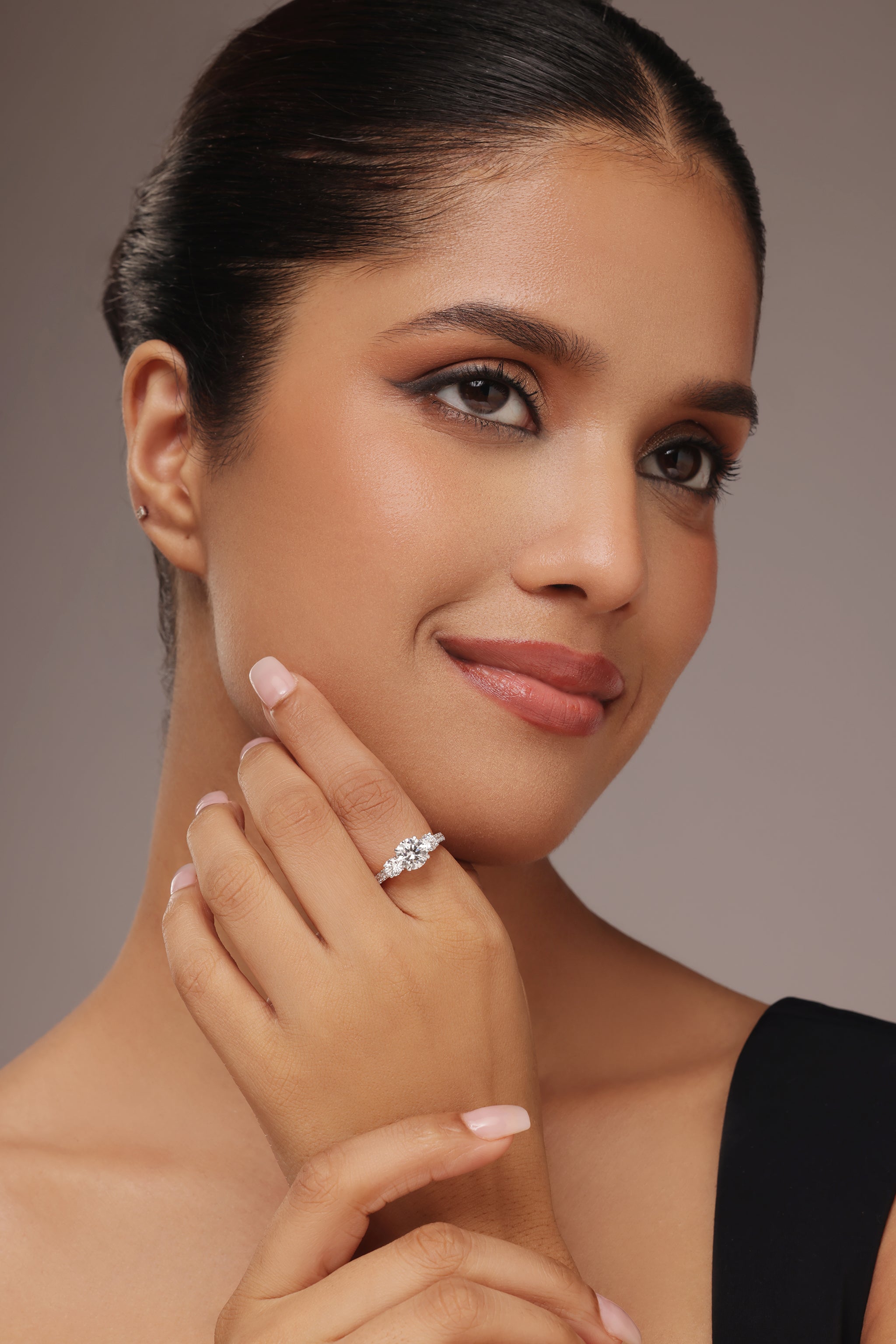 Close-up shot of a woman modeling a lab grown diamond ring featuring a three round solitaire design set on a round diamond pave band with lab grown diamond in it.