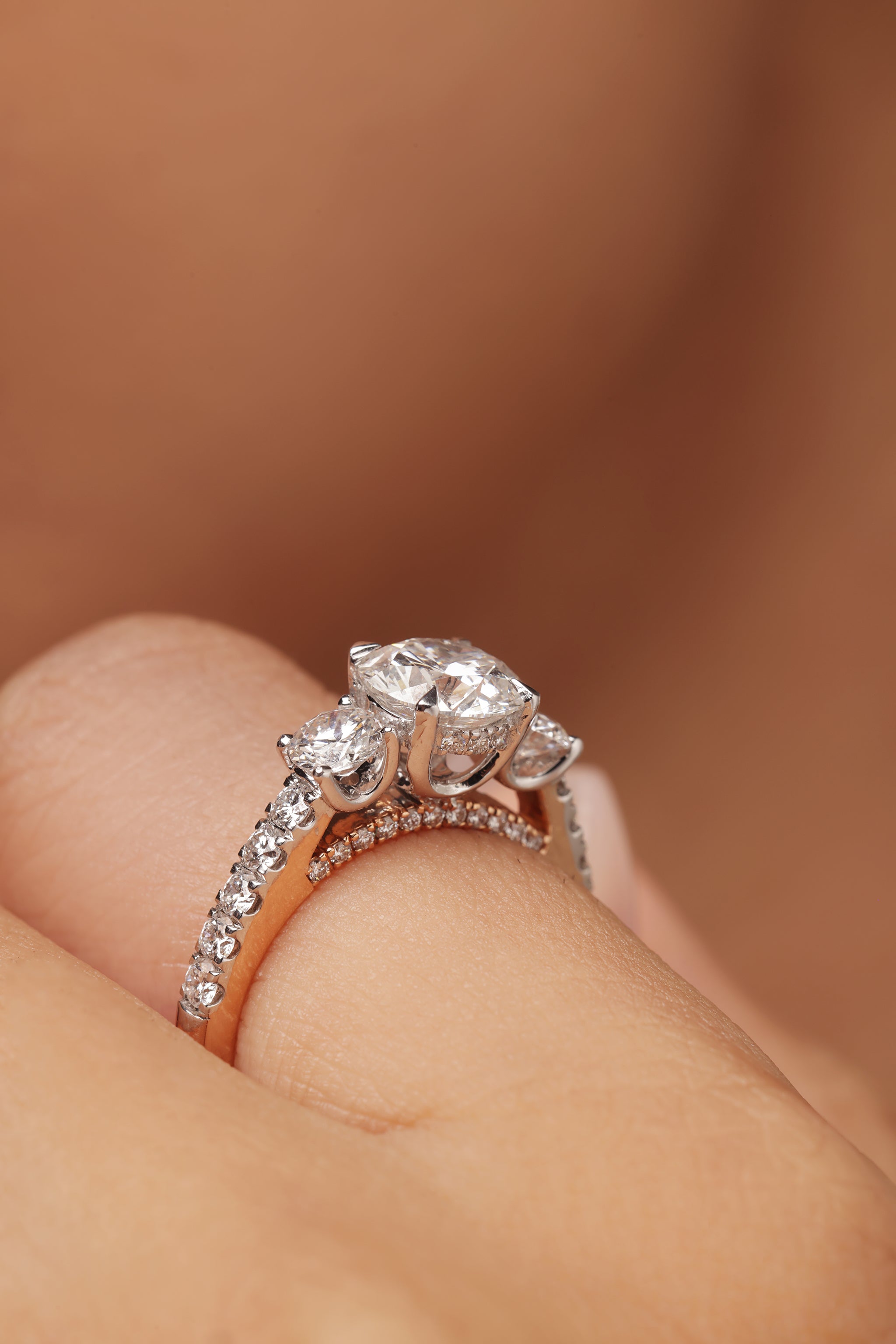 Close-up shot of a woman modeling a lab grown diamond ring featuring a three round solitaire design set in a bridge setting on a round diamond pave band with lab grown diamond in it.