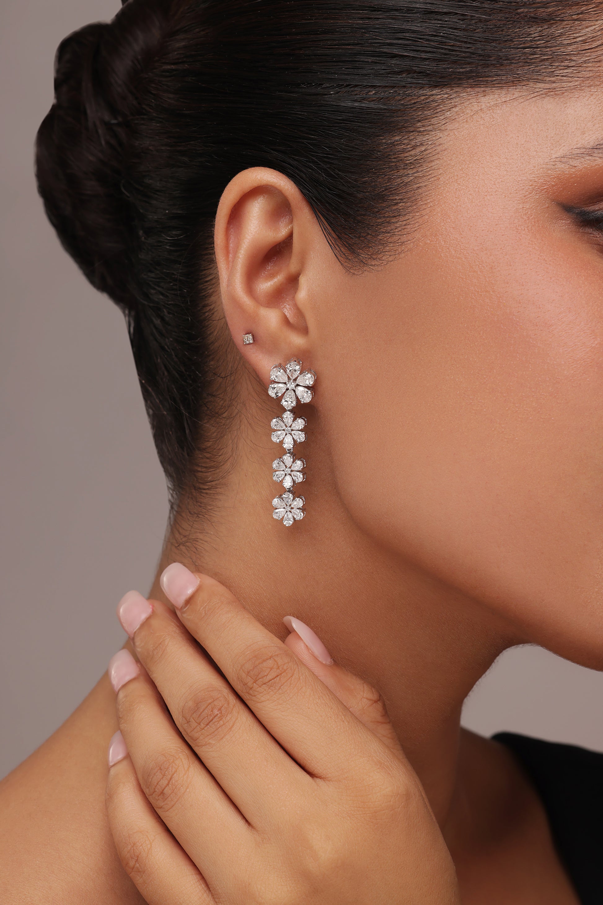 Close-up of a woman modeling long drop earrings with a floral cluster design and lab grown diamond in it, featuring four consecutive clear stone flower motifs.