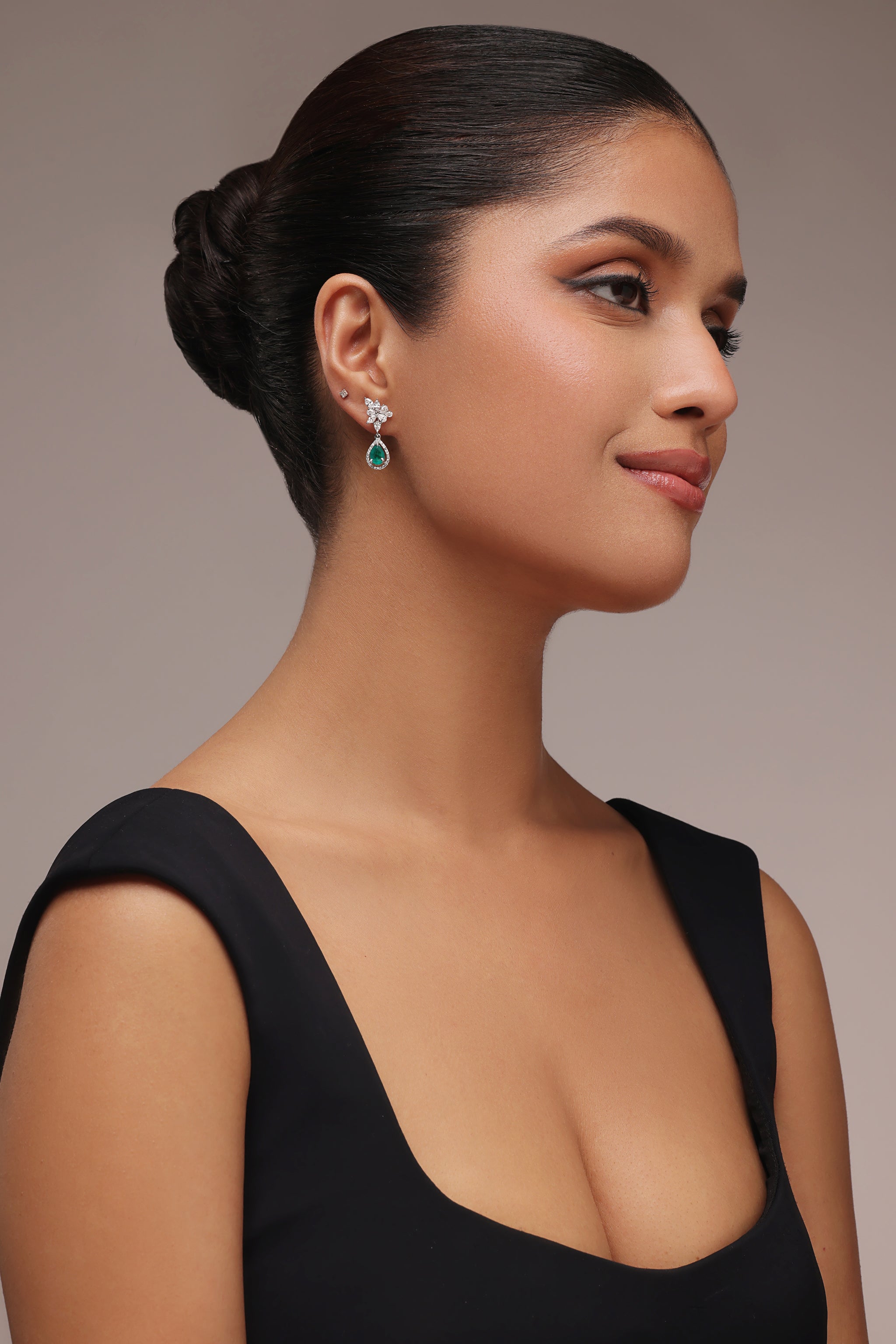 Close-up side portrait of a woman wearing a black top and drop earrings featuring a cluster of clear stones above a teardrop-shaped green stone.