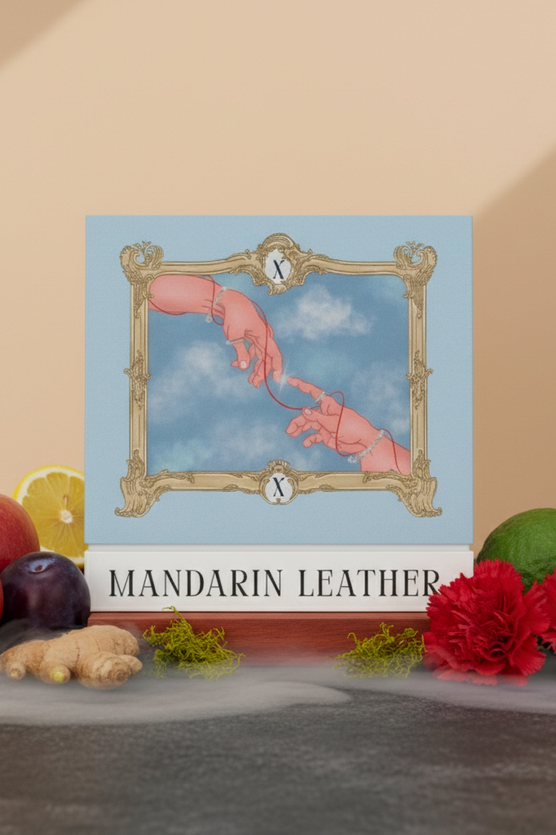 Digital art illustration on the Mandarin Leather perfume box, inspired by Michelangelo's 'Creation of Adam,' depicting two hands reaching for each other and connected by a red string, framed by a baroque border. The box is set on a display surrounded by fragrance notes like ginger, lemon, and red flowers. Represents the XAZINA brand story of connection and luxury.