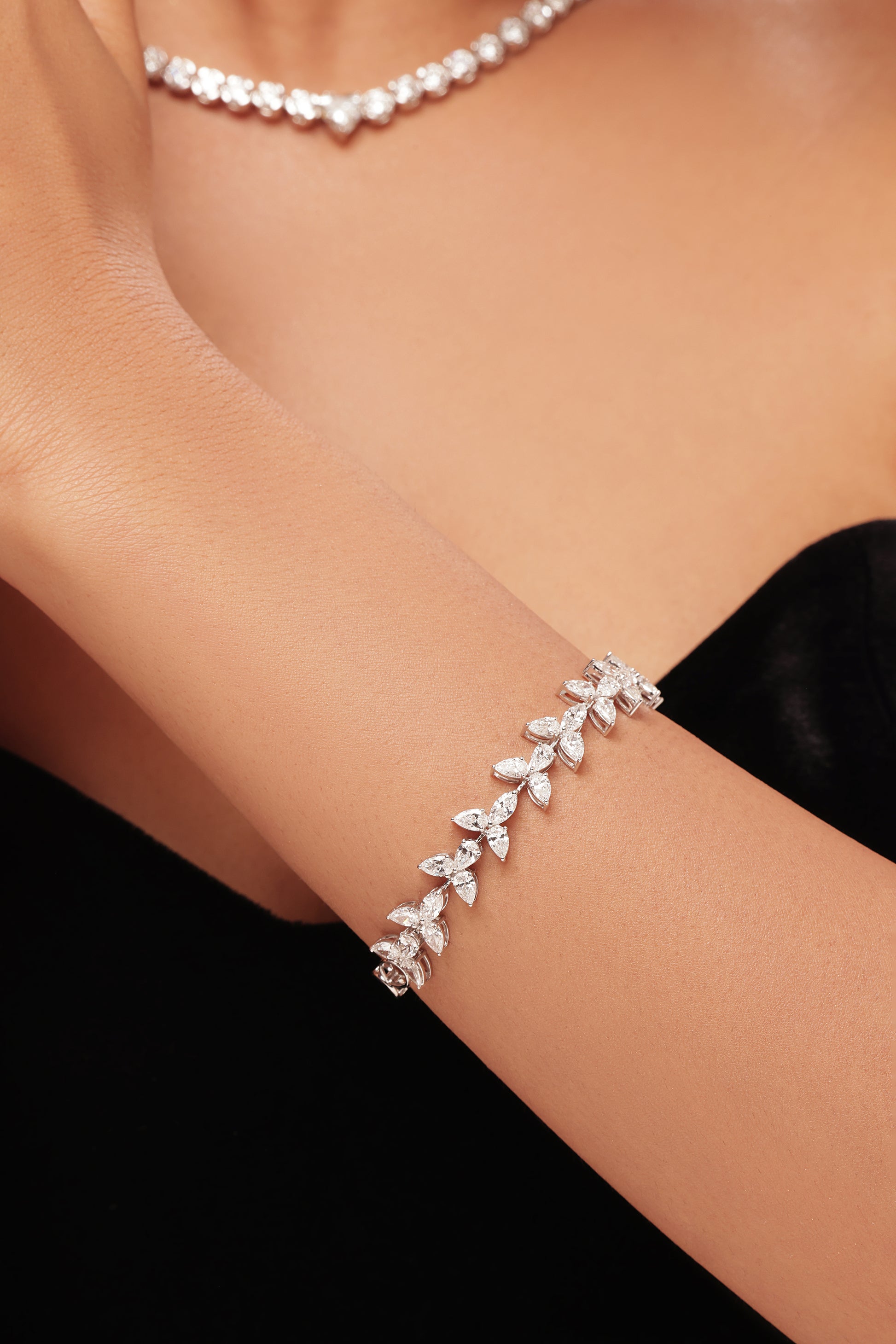 Close-up of a woman's wrist wearing a white gold or platinum bracelet, featuring a continuous link design of small, sparkling pear-shaped lab-grown diamonds. Ideal for showcasing elegant, ethical fine jewellery and diamond tennis bracelets.