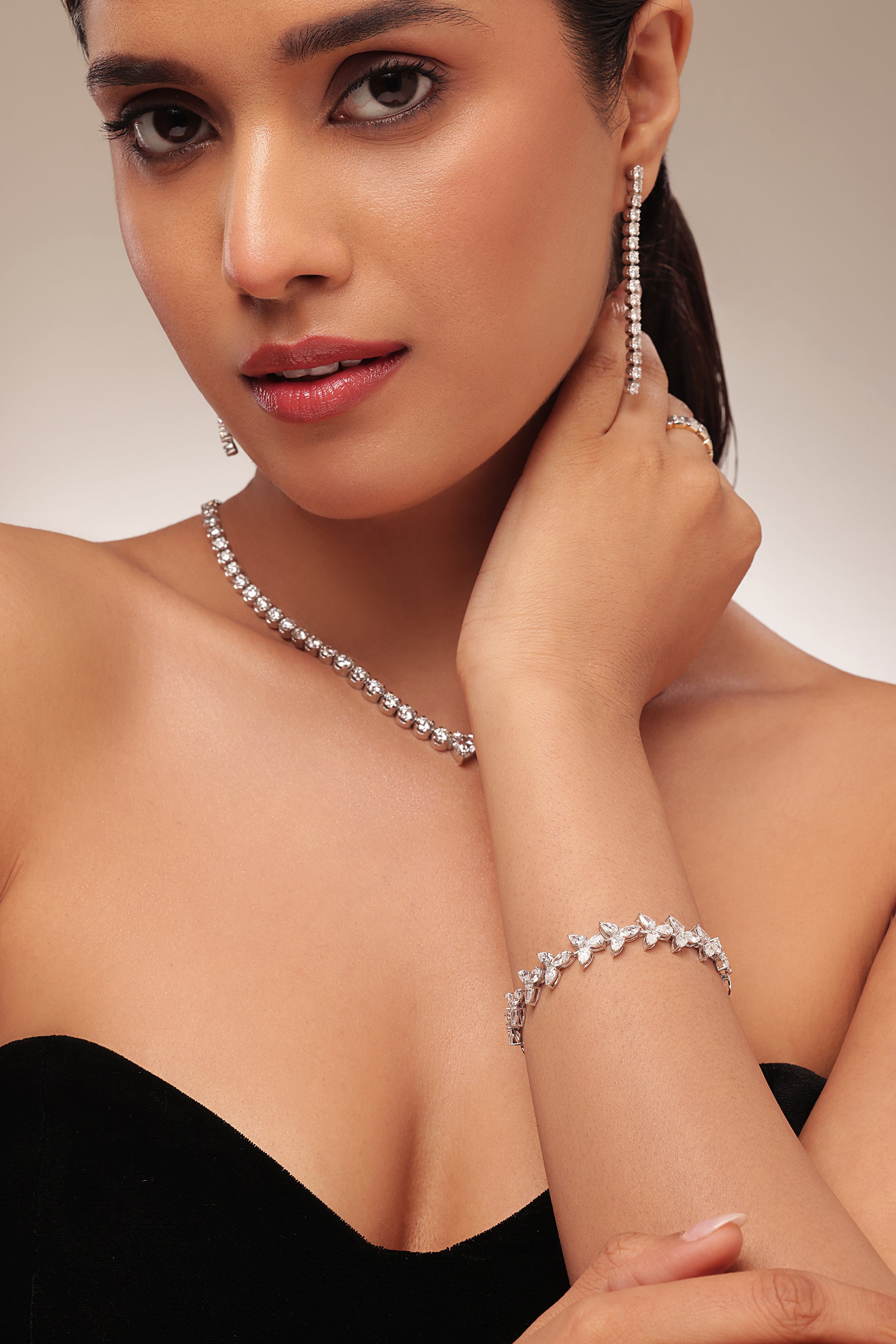 Close-up headshot of a woman wearing a delicate lab diamond tennis necklace, matching dangle earrings, and a flower-cluster lab diamond bracelet. Ideal for showcasing luxury lab diamond jewellery sets and formal wear accessories.