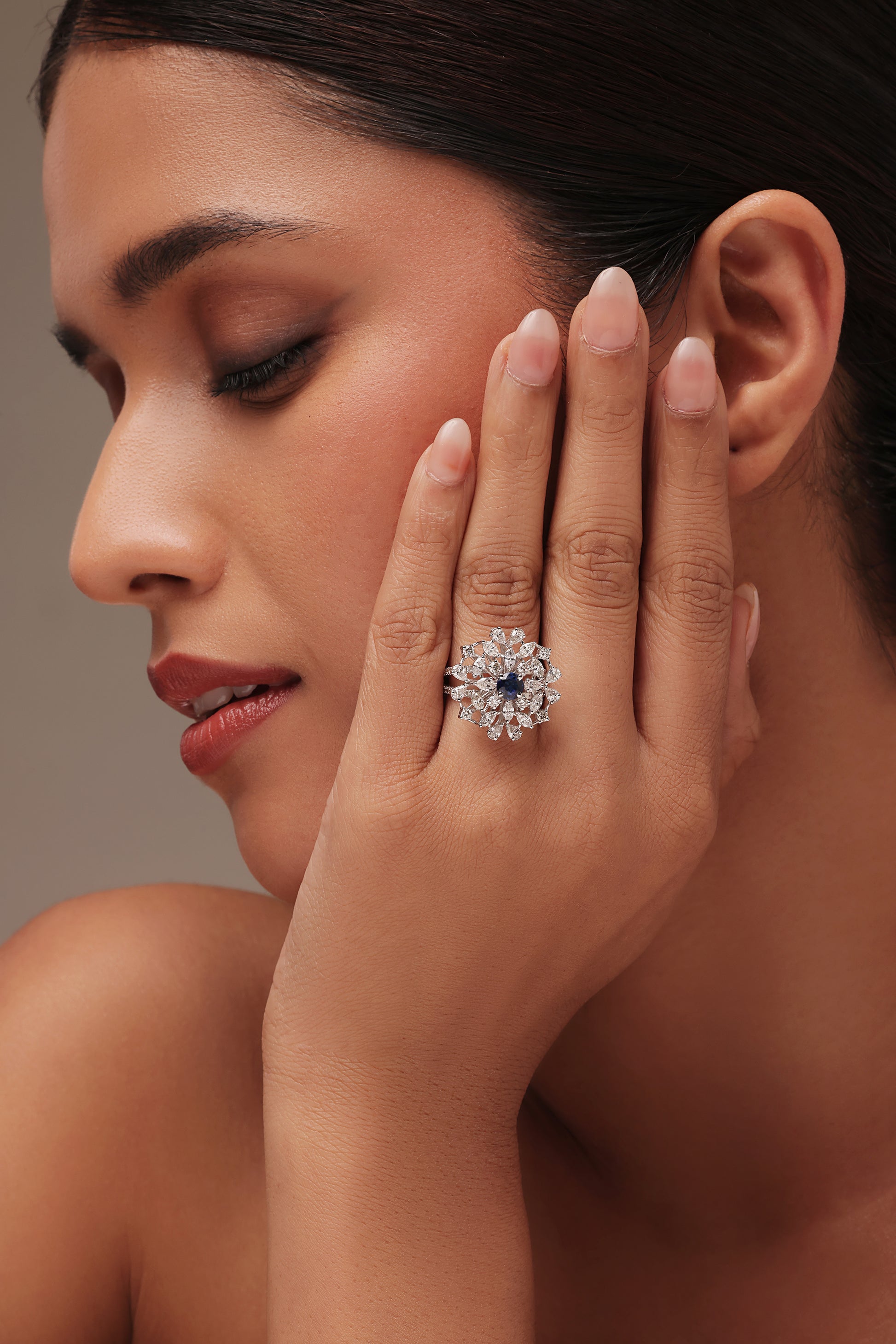 Close-up shot of a hand modeling a brilliant cluster ring with lab grown diamond in it, featuring a central oval blue stone surrounded by a starburst of clear pear diamond accents.