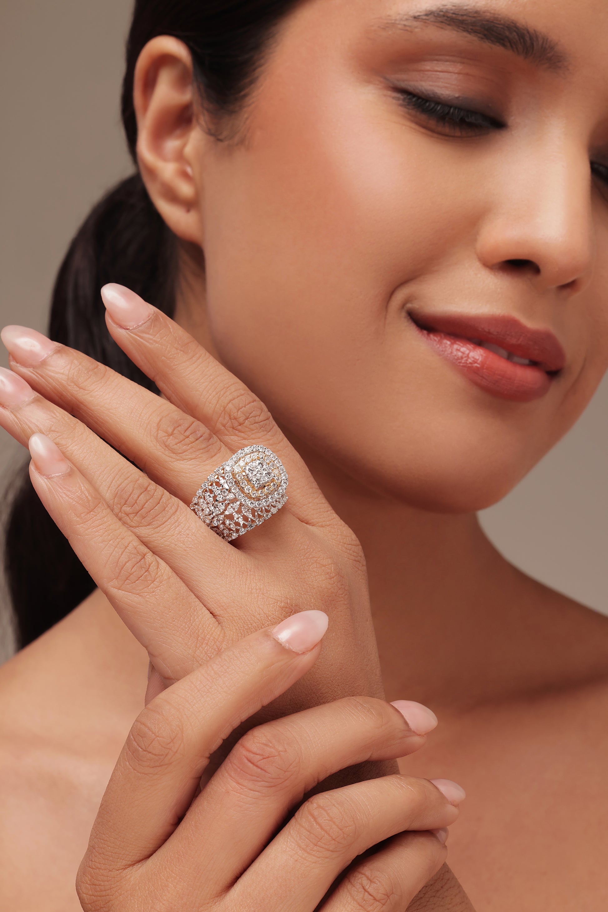 Close-up shot of a hand modeling an oversized cocktail ring with lab grown diamond in it. The intricate piece features a multi-layered design that includes a central round diamond area with a double halo and a wide band accented with a mini marquise diamond pattern on the band.