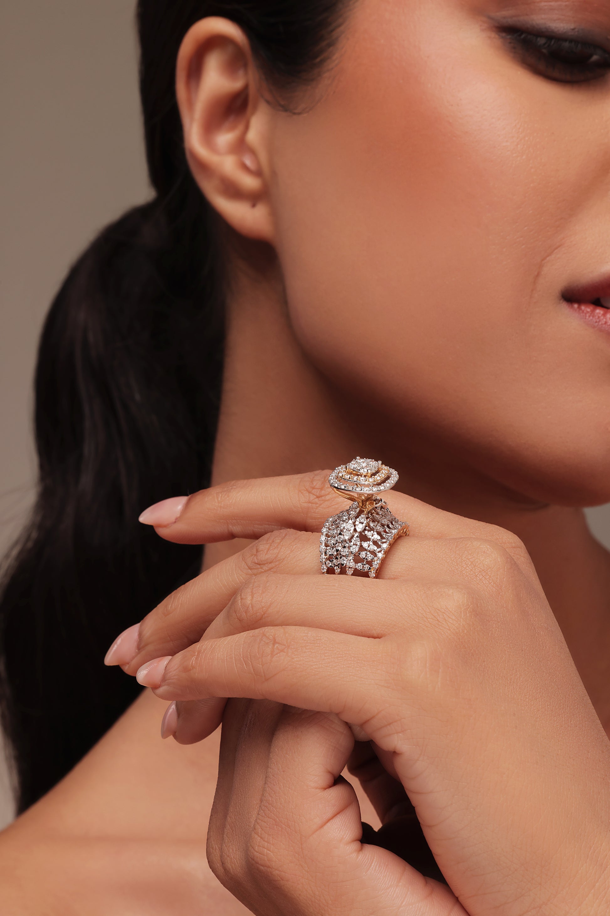 Close-up shot of a hand modeling an oversized cocktail ring with lab grown diamond in it. The intricate piece features a multi-layered design that includes a central round diamond area with a double halo and a wide band accented with a mini marquise diamond pattern on the band.