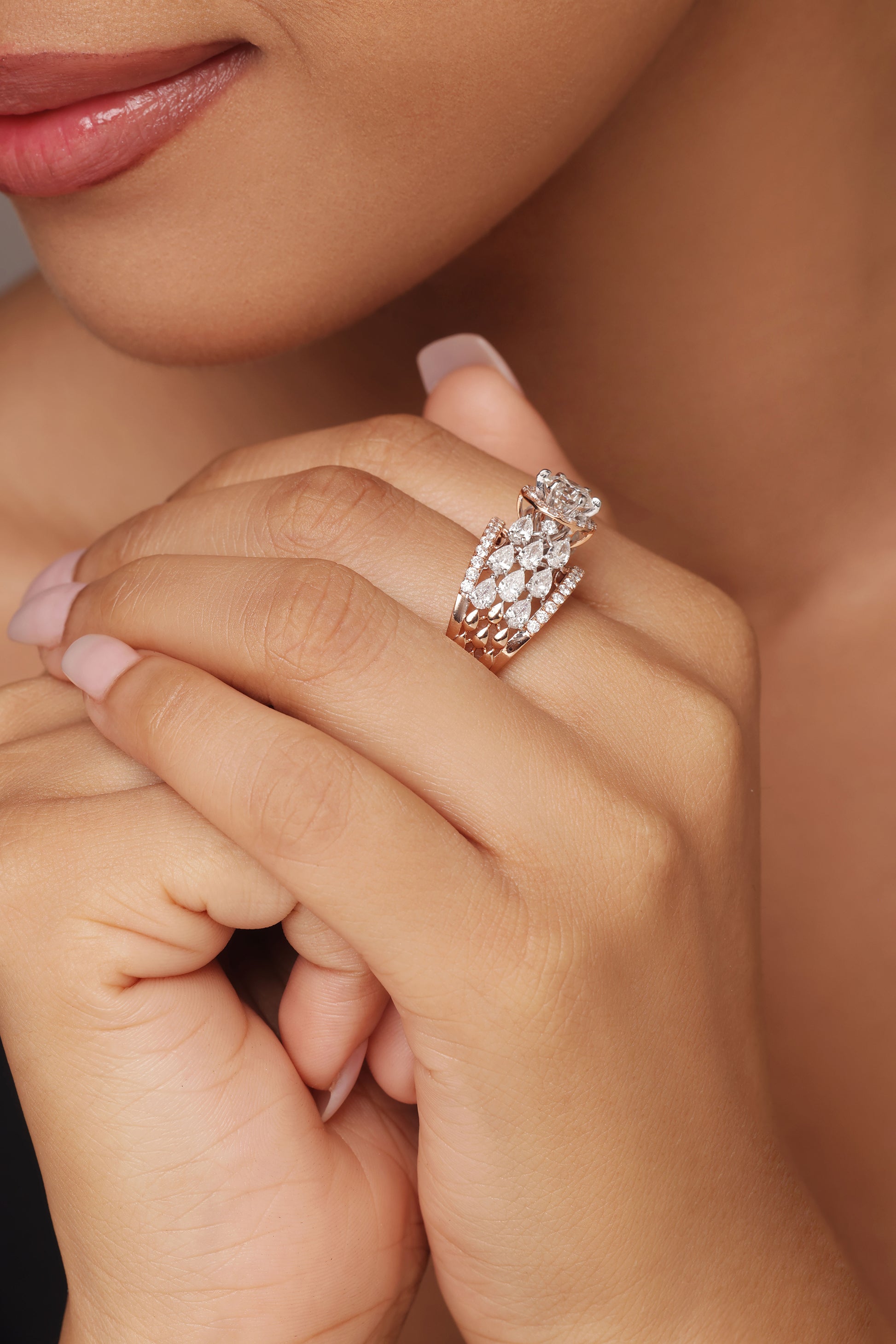 Close-up shot of a hand modeling a luxurious ring with lab grown diamond in it. The design features a cluster that gives the effect of a round diamond with halo, and is surrounded by smaller, dazzling clusters that act as pear accents, all set on a rose gold pavé band.