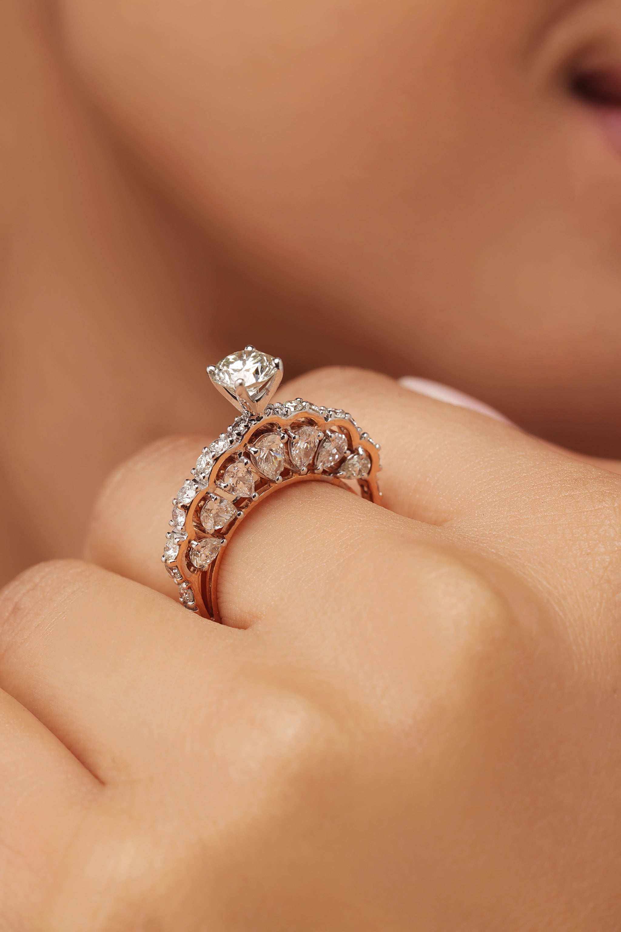 Close-up shot of a hand modeling a spectacular ring with a round diamond center stone and lab grown diamond in it. The design features a pavé round diamond on the band and large, scalloped accents on the sides resembling pear diamond shapes.