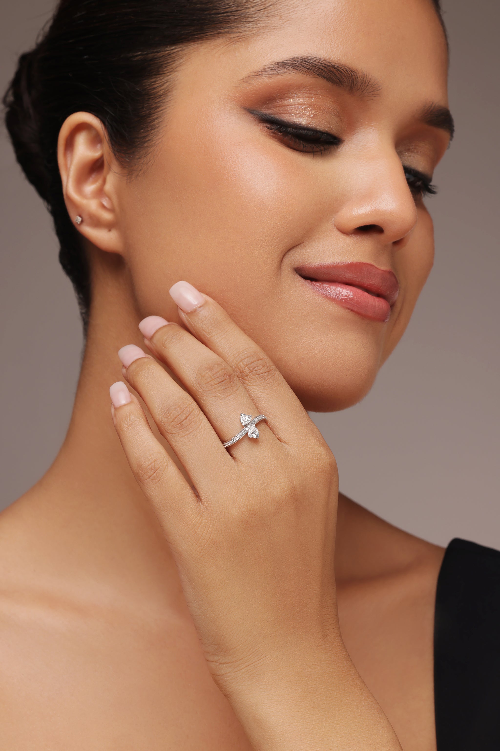 Close-up of a woman's hand showcasing a unique two-stone bypass ring set in white gold or platinum, featuring 2 heart lab-grown diamonds in the center. The band is encrusted with sparkling pavé diamonds. Ideal for a modern, romantic ethical engagement ring or cocktail ring.