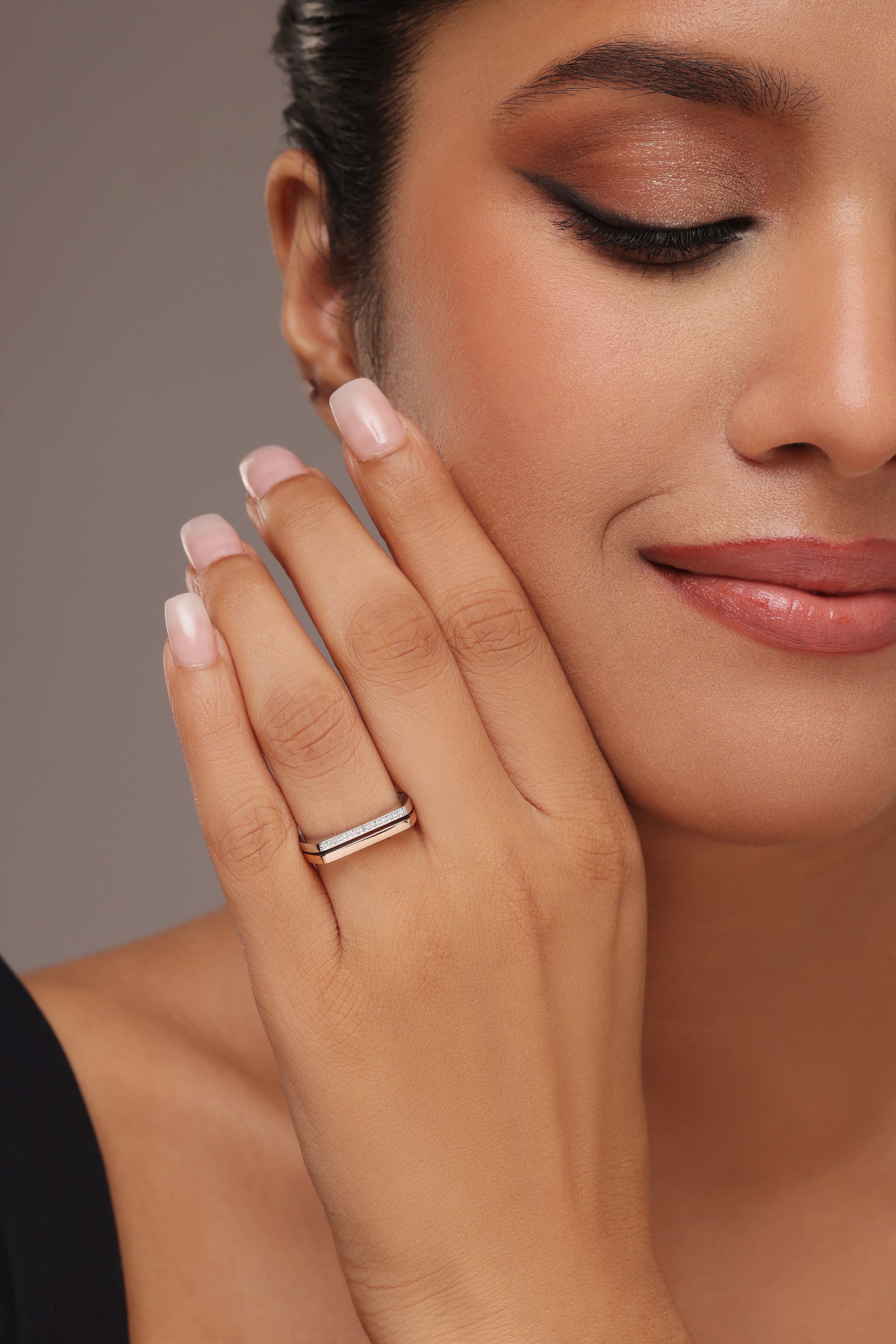 Close-up of a woman's hand, subtly touching her face, showcasing a delicate rose gold lab diamond band ring. The ring features two parallel rows of shimmering pavé set lab-grown diamonds, making it ideal for wedding bands, stacking rings, or everyday ethical fine jewellery.