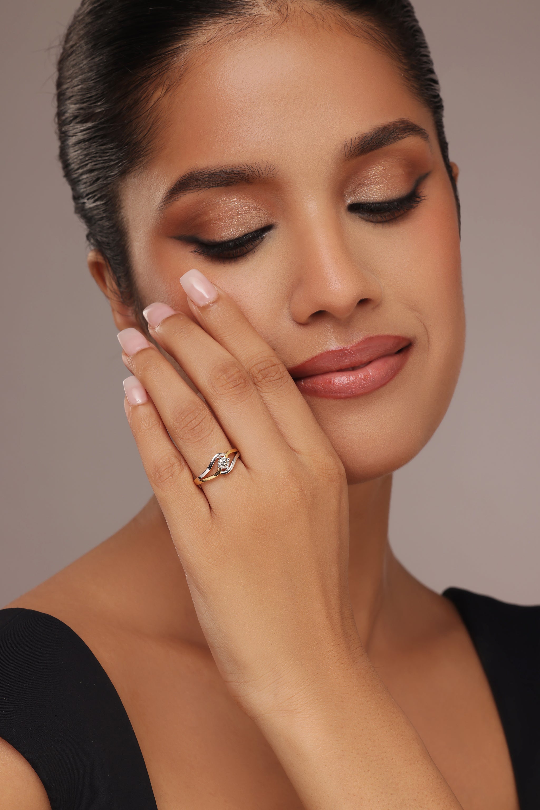 Close-up shot of a hand modeling a modern two-tone ring with a round diamond center stone, set within a swirling gold and silver band, featuring lab grown diamond in it.