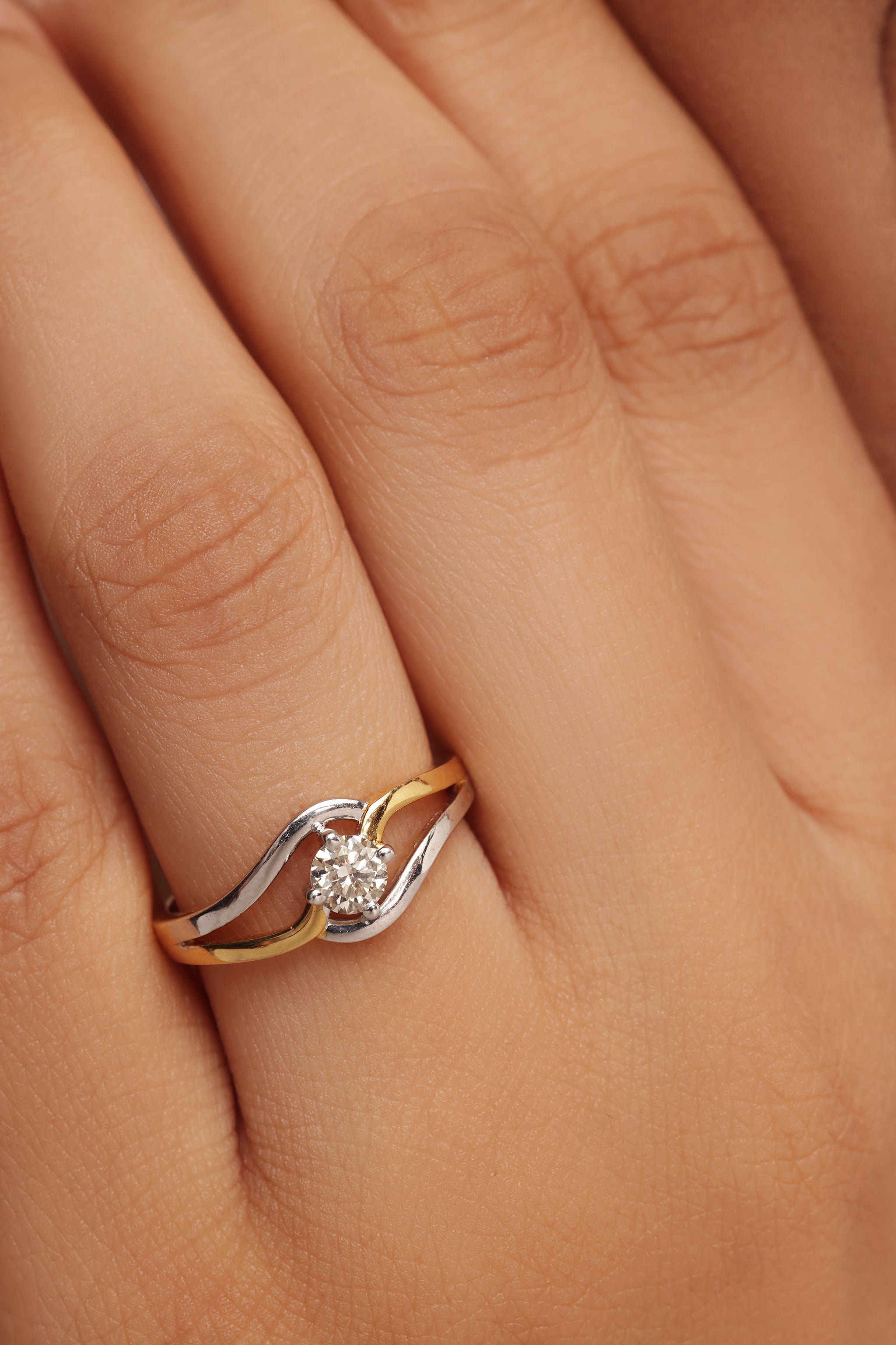 Close-up shot of a hand modeling a modern two-tone ring with a round diamond center stone, set within a swirling gold and silver band, featuring lab grown diamond in it.