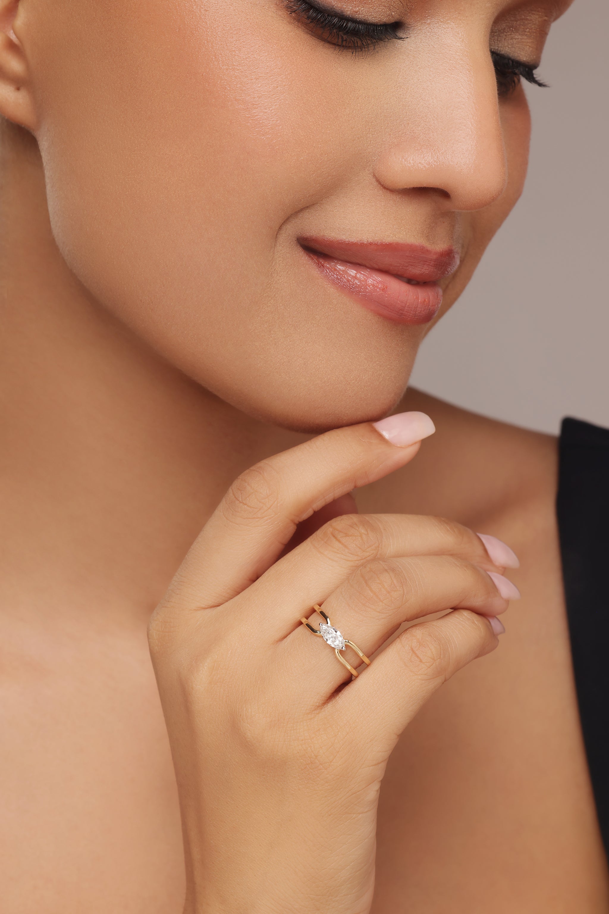 Close-up shot of a hand modeling a yellow gold ring featuring a horizontal marquise diamond center stone set in a simple, open bypass band with lab grown diamond in it.