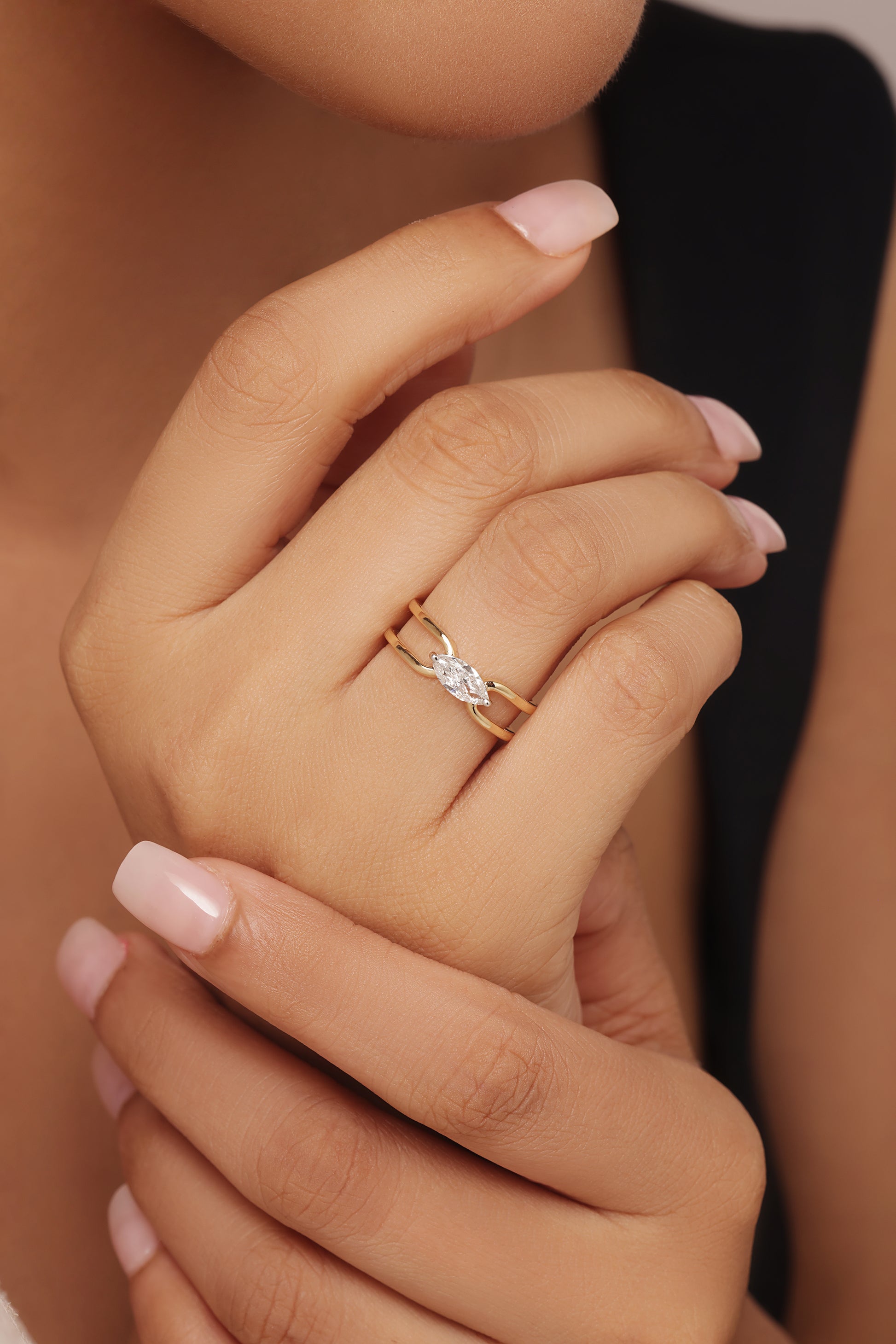 Close-up shot of a hand modeling a yellow gold ring featuring a horizontal marquise diamond center stone set in a simple, open bypass band with lab grown diamond in it.