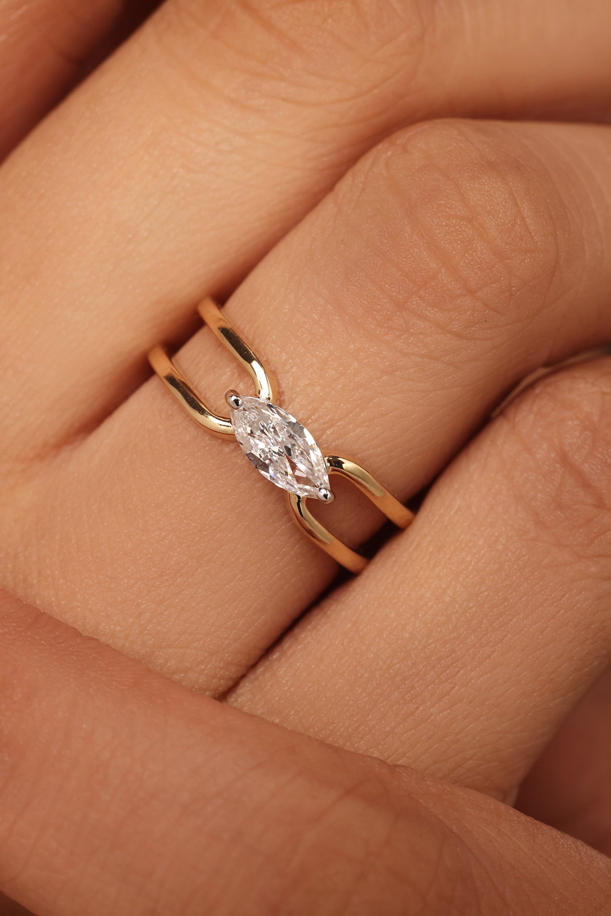 Close-up shot of a hand modeling a yellow gold ring featuring a horizontal marquise diamond center stone set in a simple, open bypass band with lab grown diamond in it.