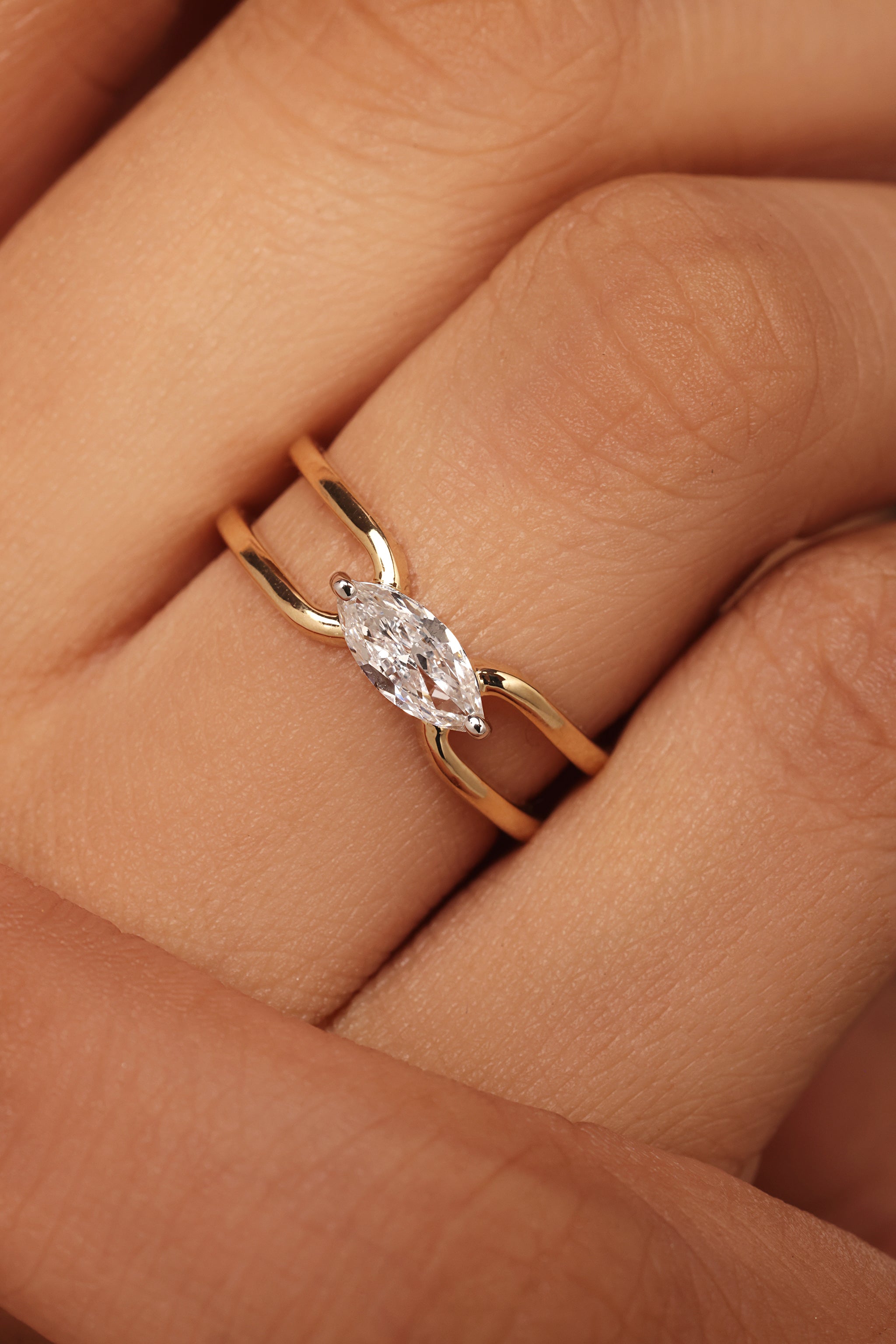 Close-up shot of a hand modeling a yellow gold ring featuring a horizontal marquise diamond center stone set in a simple, open bypass band with lab grown diamond in it.